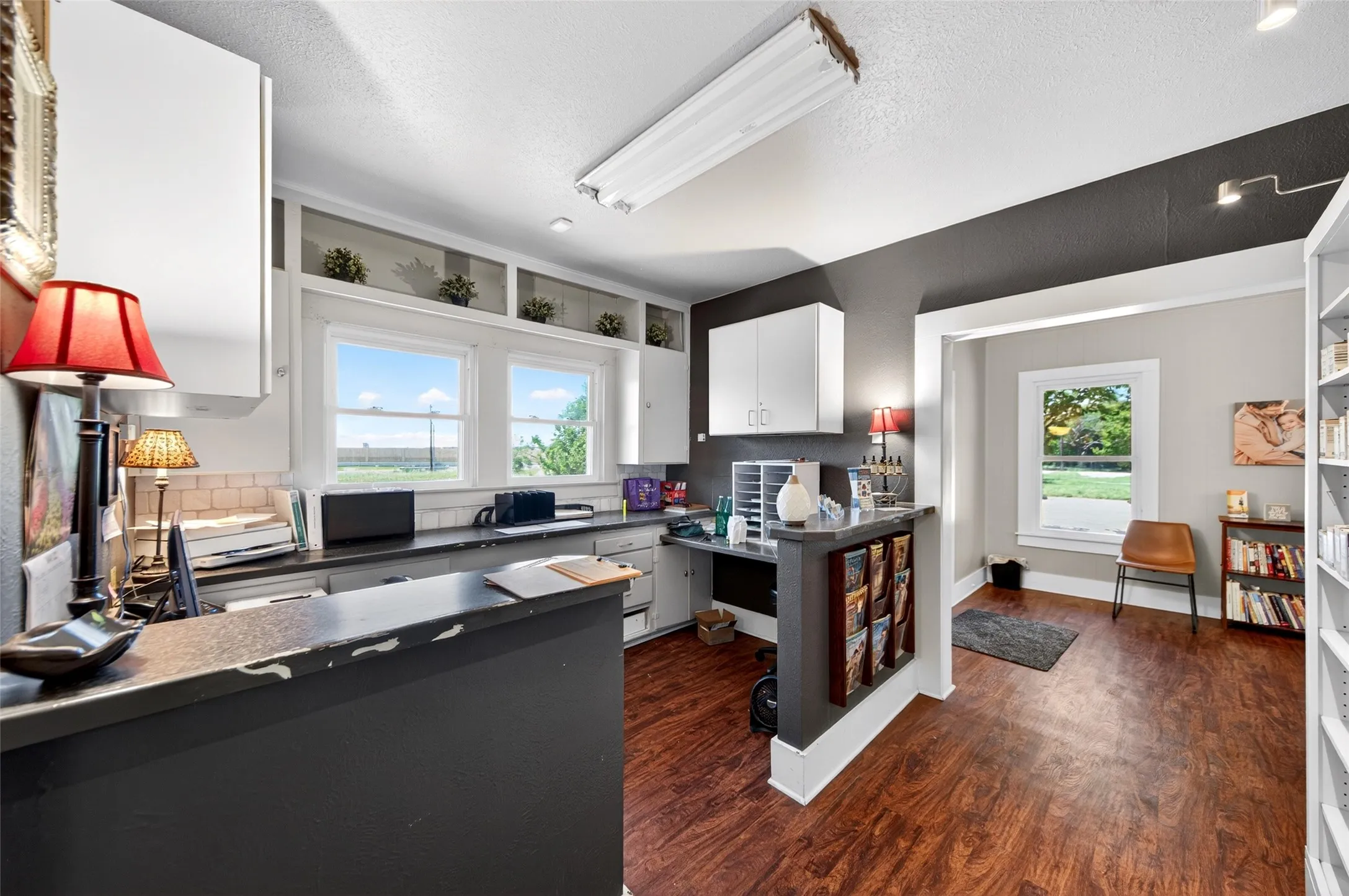 Wood-finish flooring, built-in shelving, white cabinetry, dark countertops, and light-colored wall paint