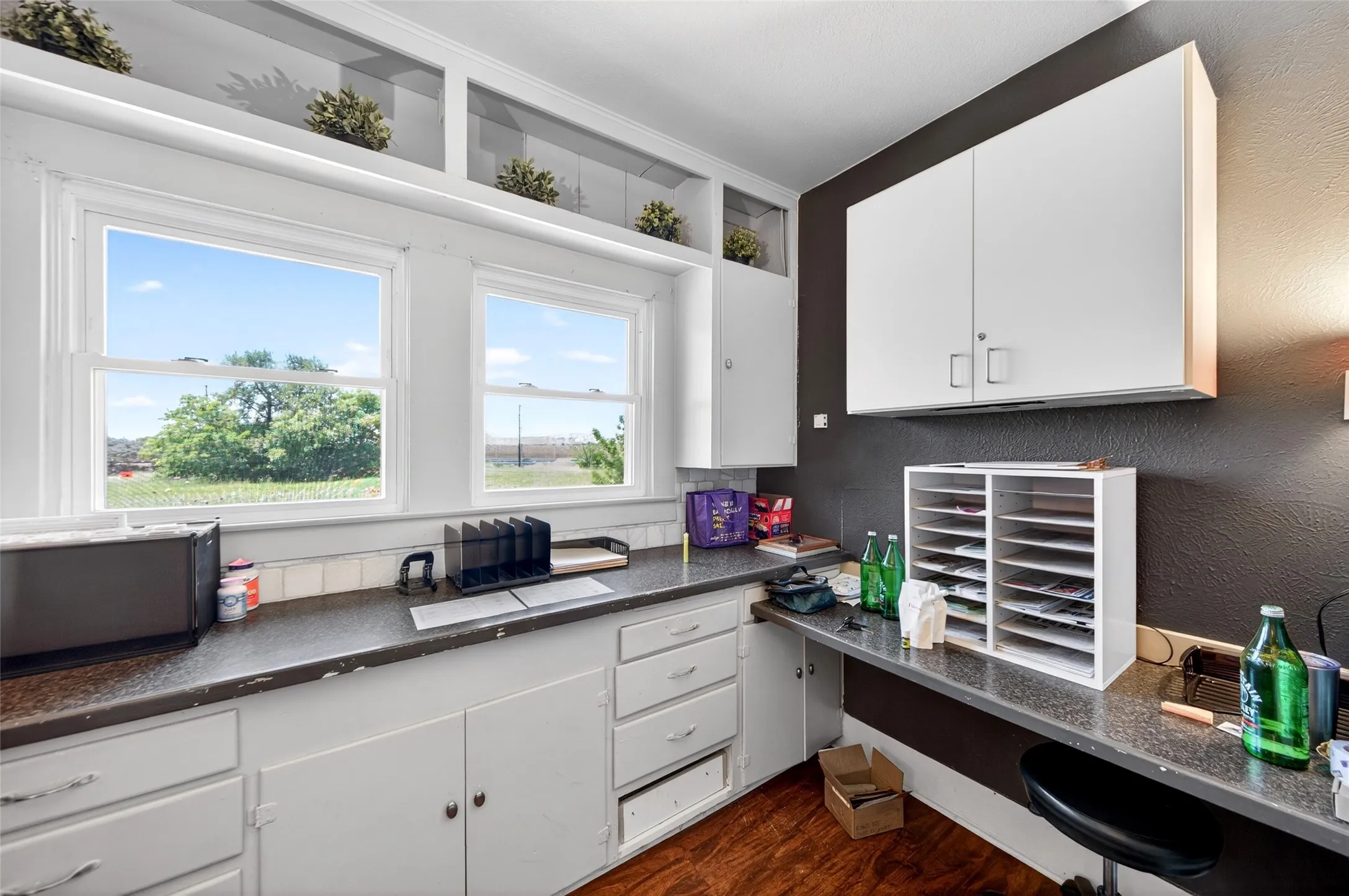 Dual windows, built-in shelving, white cabinetry, dark countertops, and wood-finish flooring