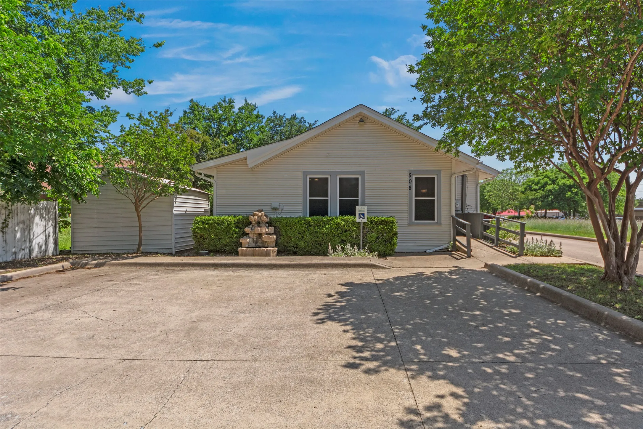 White siding exterior with a gable roof, concrete parking area, and a stone water feature
