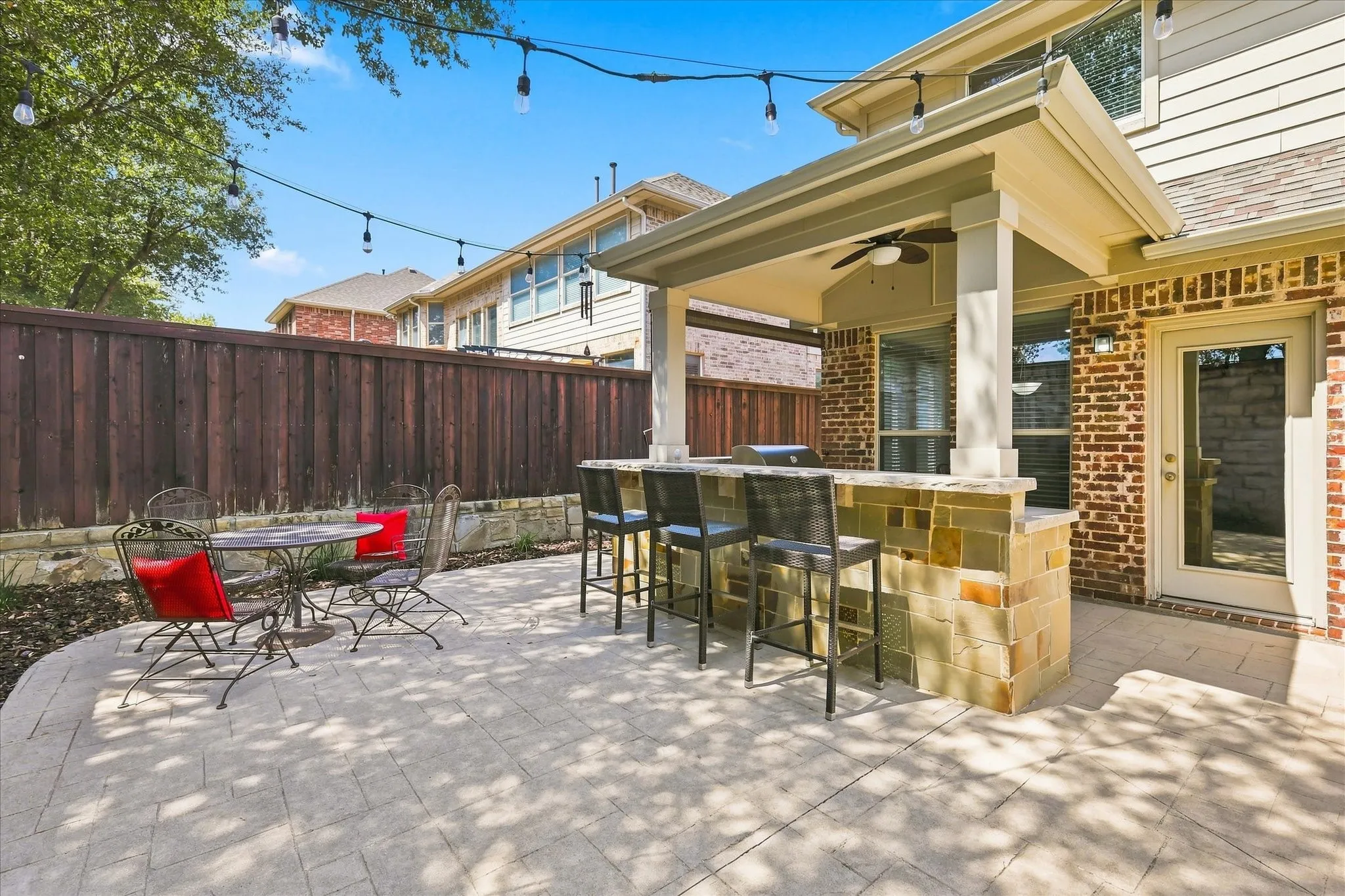 Paved patio featuring a built-in outdoor kitchen with bar seating, a covered area with a ceiling fan, and brick exterior detailing