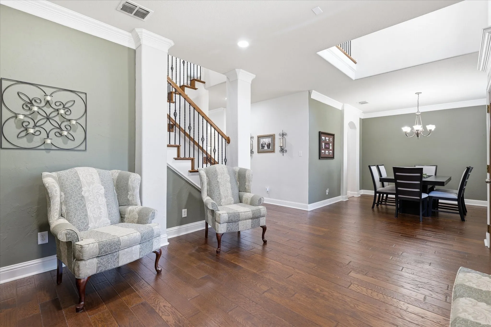 Hardwood flooring, crown molding, staircase with wrought iron balusters, and a dining area with a chandelier