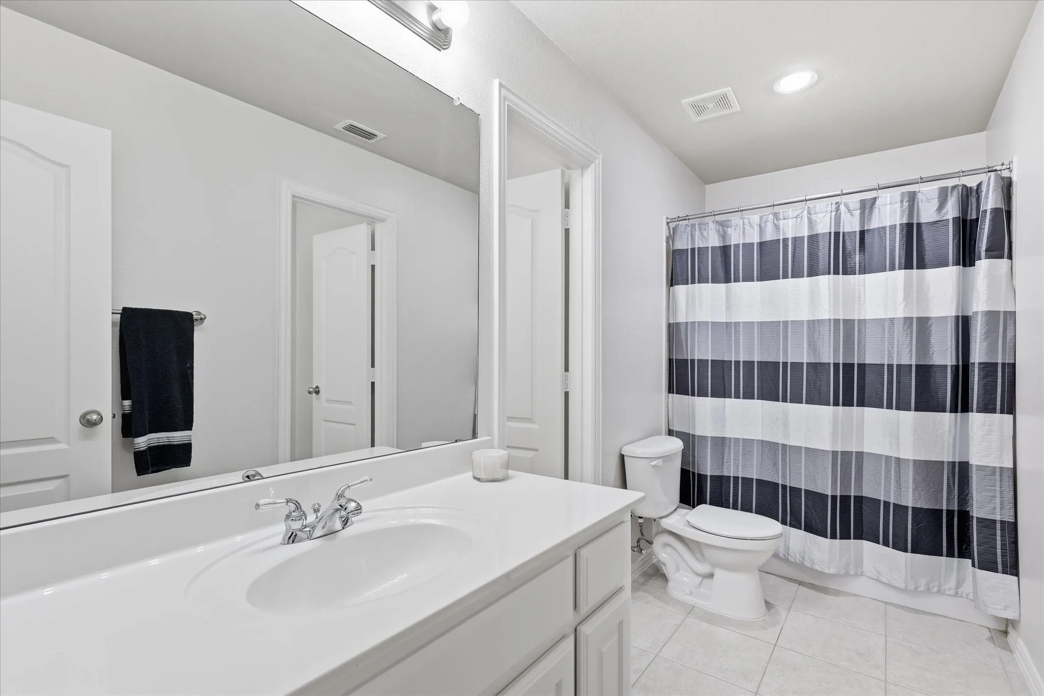 Bathroom featuring a single vanity with integrated sink, chrome faucet, wall-mounted mirror, white paneled cabinetry, and tile flooring