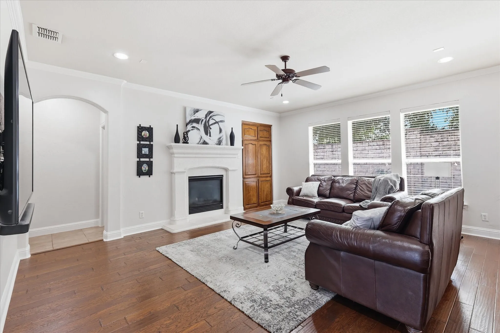 Spacious living area featuring wood-finish flooring, a white mantel fireplace, recessed lighting, and a ceiling fan