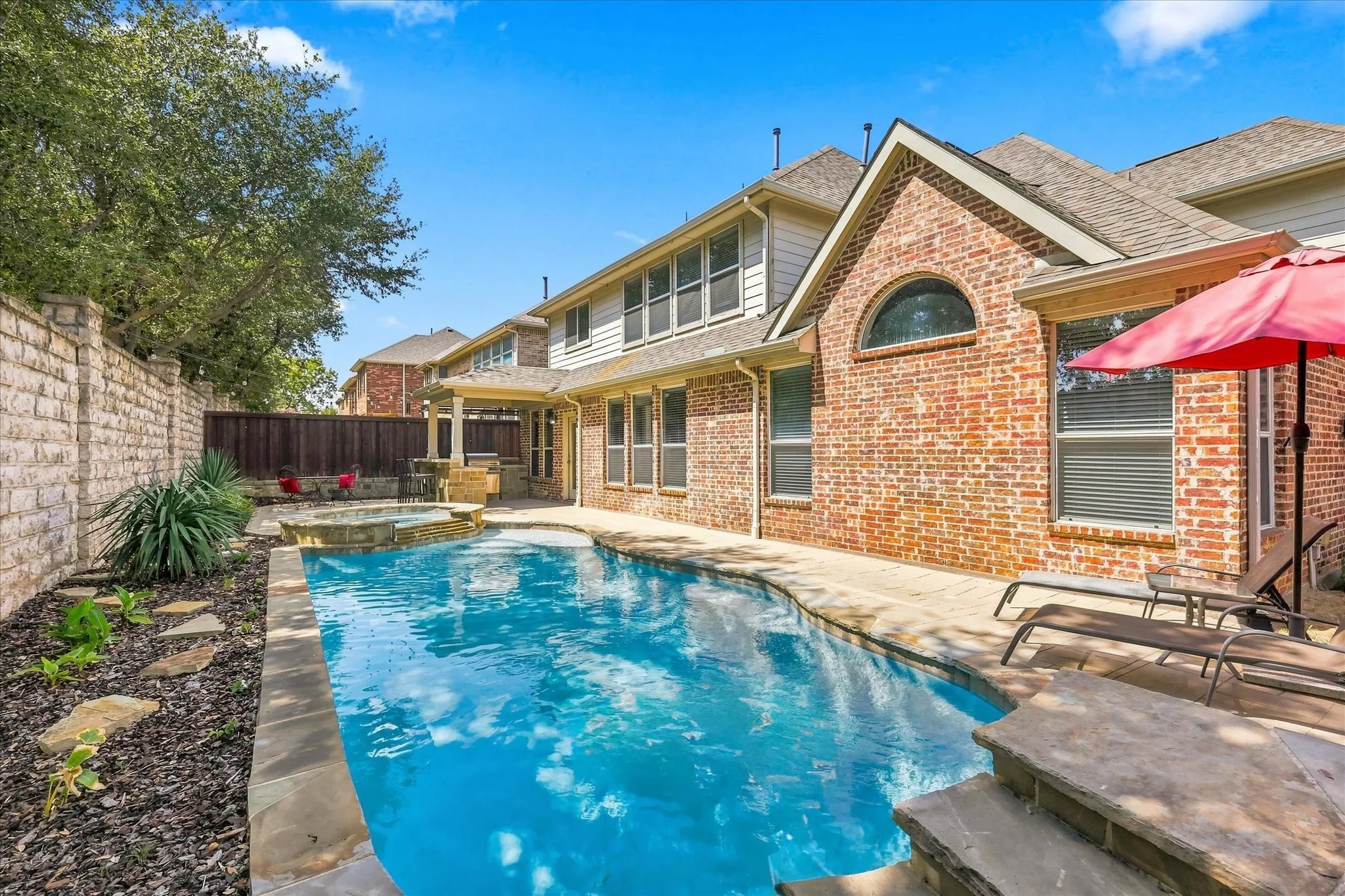 Brick and siding exterior with arched window, curved swimming pool, integrated spa, stone coping, and paved patio