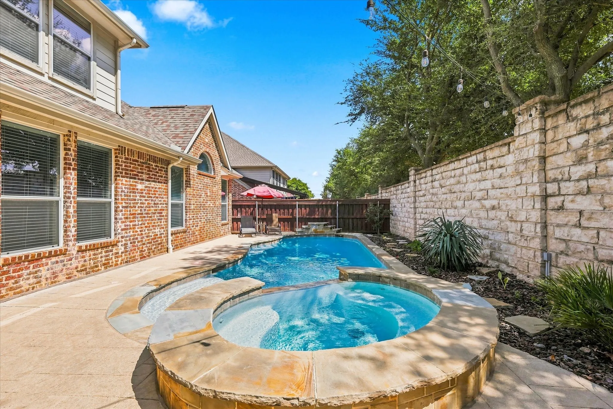 Brick exterior with gabled roofline, featuring a swimming pool, integrated spa, and stone retaining wall