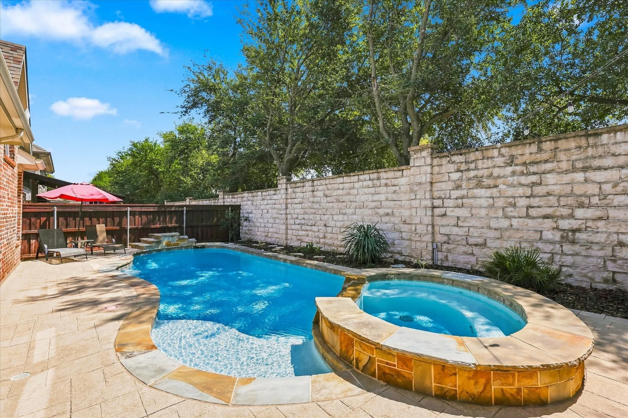 Resort-style pool with integrated spa, paver patio, stone retaining wall, and mature trees