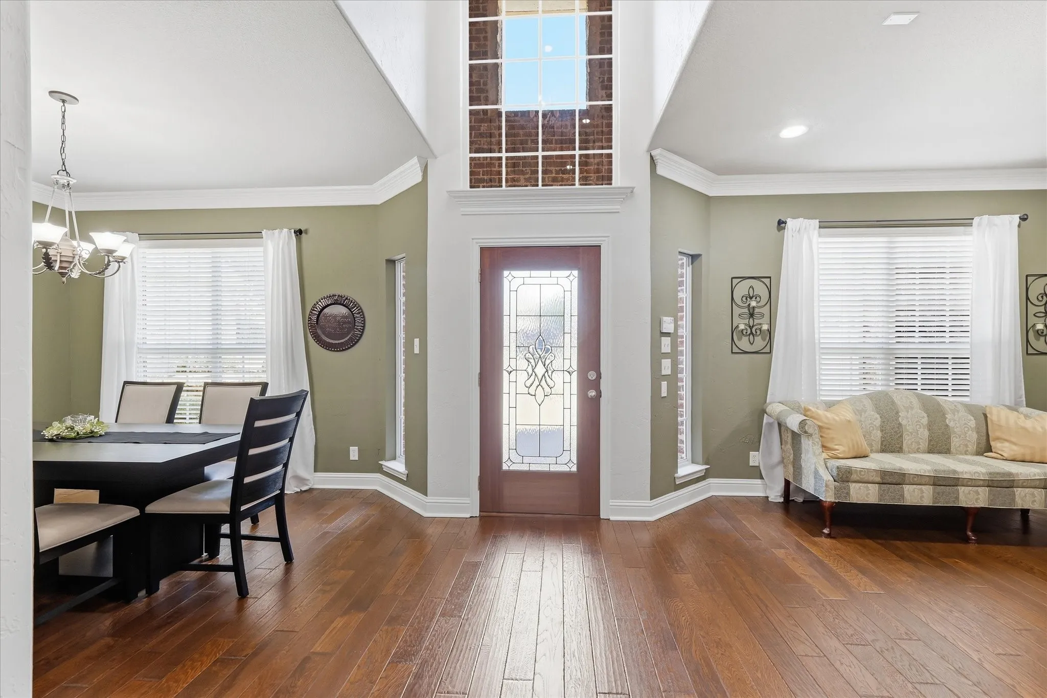 Hardwood-style flooring throughout, high ceilings, decorative front door with leaded glass, white crown molding, and a chandelier in the dining area