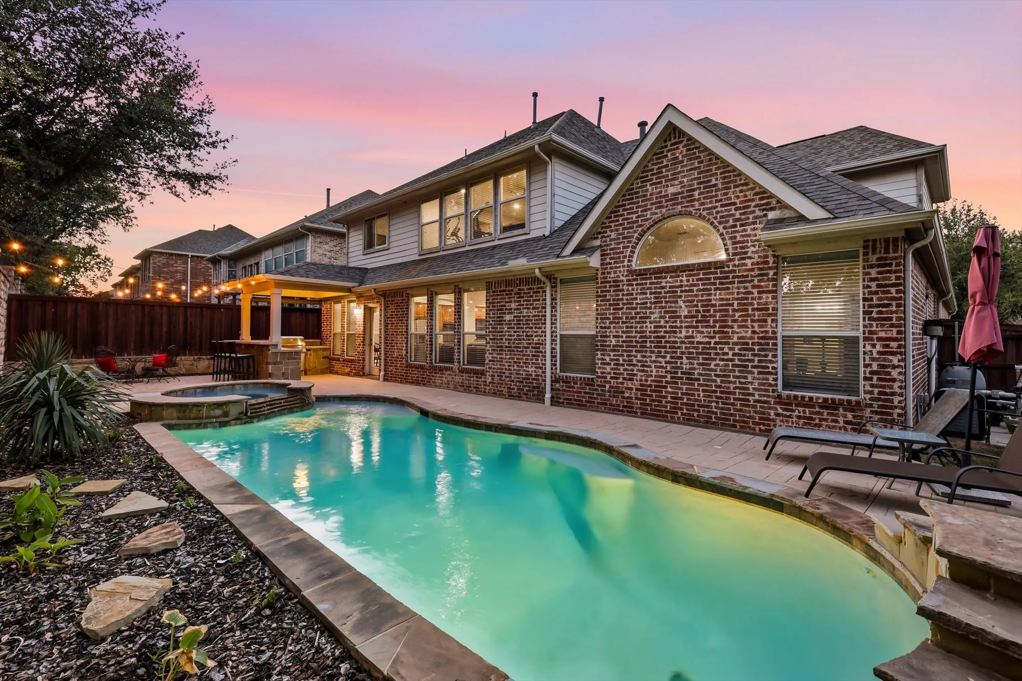 Brick exterior with siding accents, inground swimming pool with integrated spa, and an outdoor kitchen area under a covered patio