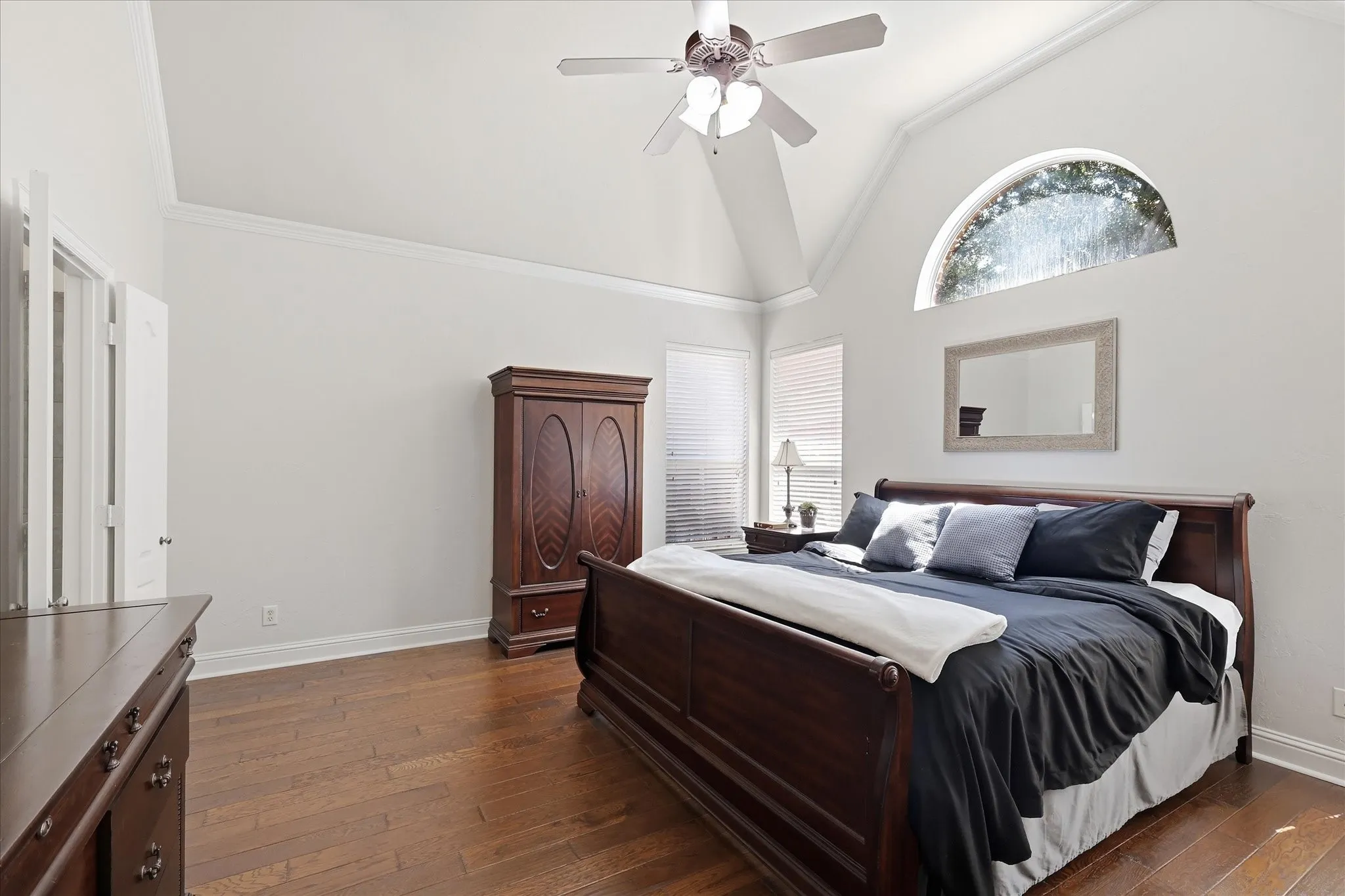 Vaulted ceiling with a ceiling fan, arched transom window, wood-finish flooring, and white interior doors