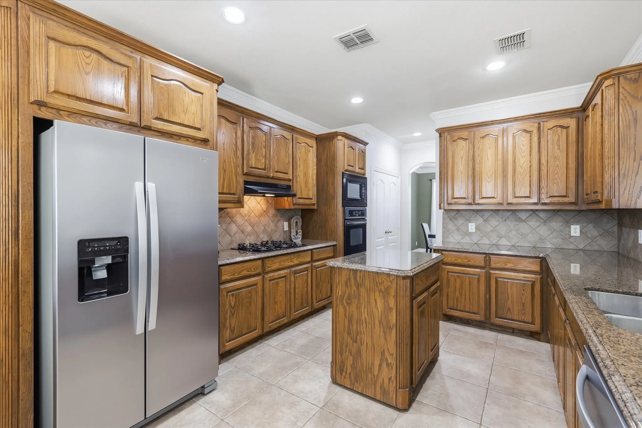 Well-appointed kitchen featuring wood cabinetry, stainless steel appliances, a center island, stone countertops, and tile flooring
