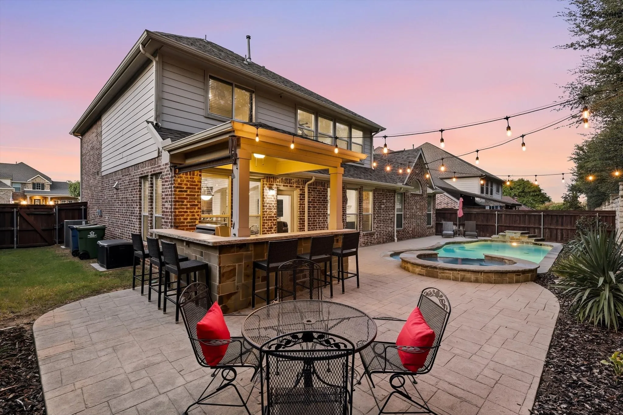 Expansive backyard featuring a built-in outdoor kitchen with bar seating, a swimming pool with an attached spa, and a paved patio area