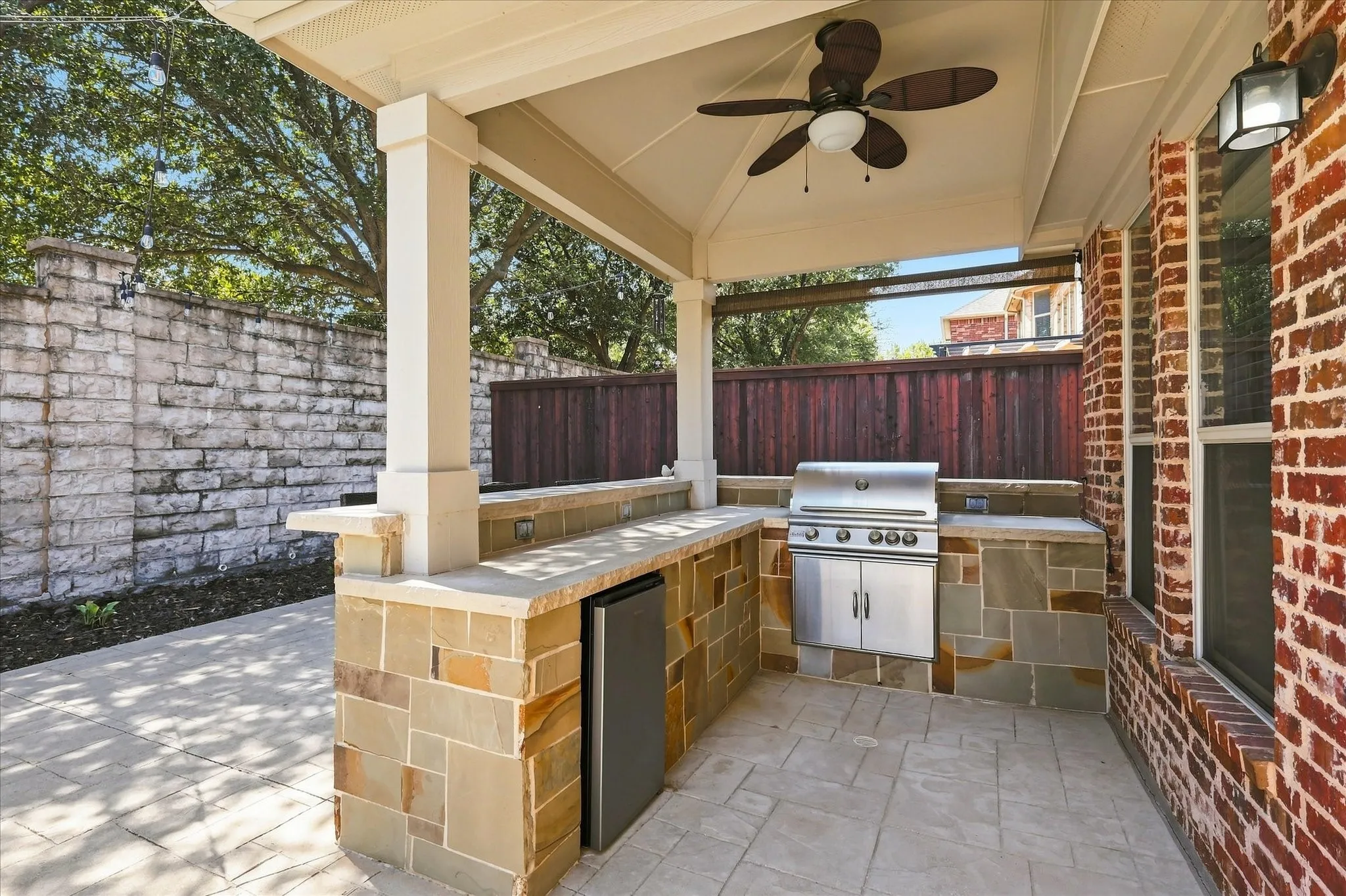 Covered outdoor living space featuring a built-in grill, stone-clad bar with an integrated refrigerator, ceiling fan, and brick exterior wall