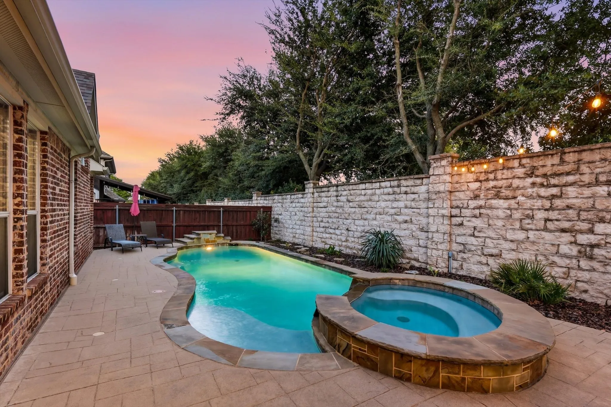 Freeform swimming pool with a stone waterfall feature, integrated spa, and expansive paved patio
