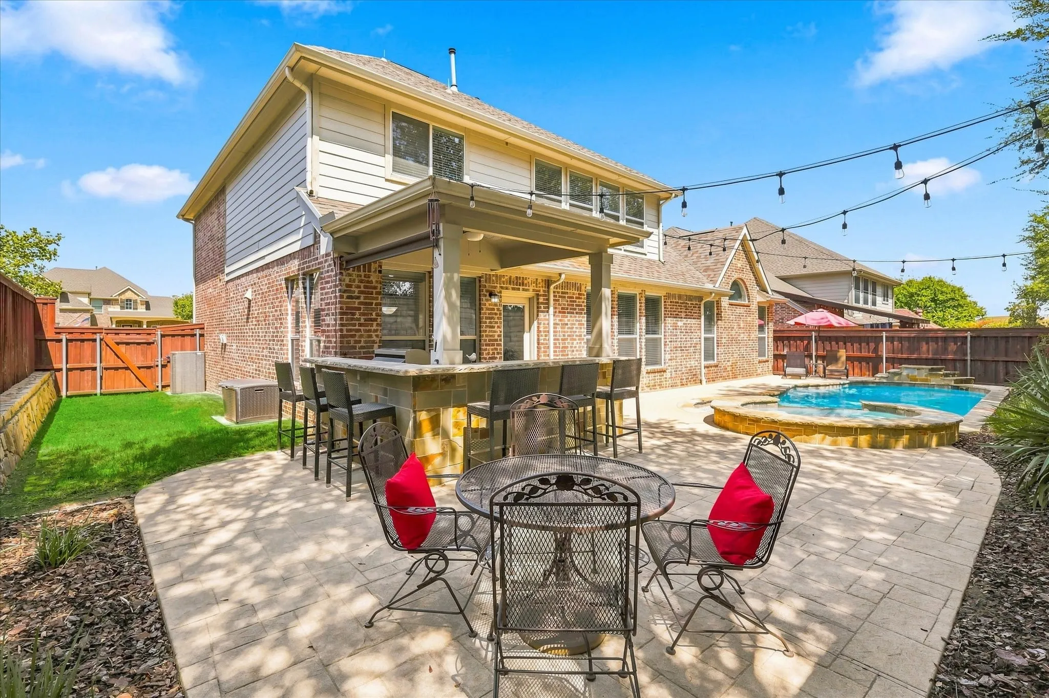 Expansive paver patio featuring a built-in outdoor kitchen with bar seating, and a swimming pool with an integrated spa