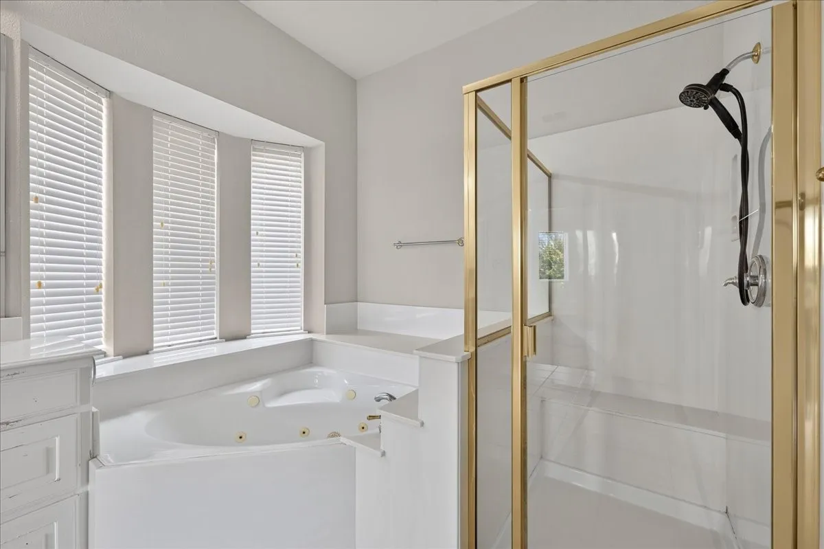 Soaking tub with jets, framed glass shower enclosure, multiple windows with blinds, and a built-in vanity