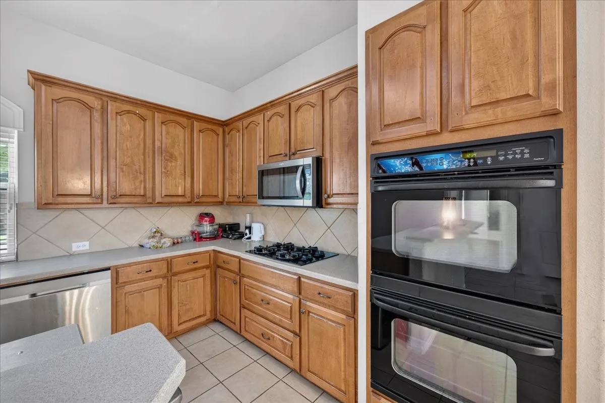 Kitchen featuring wood cabinetry, stainless steel microwave, gas cooktop, double wall ovens, and tile flooring