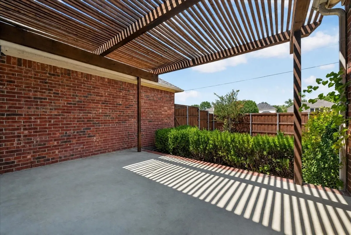 Concrete patio with a wood-slat pergola, brick exterior, and a privacy fence