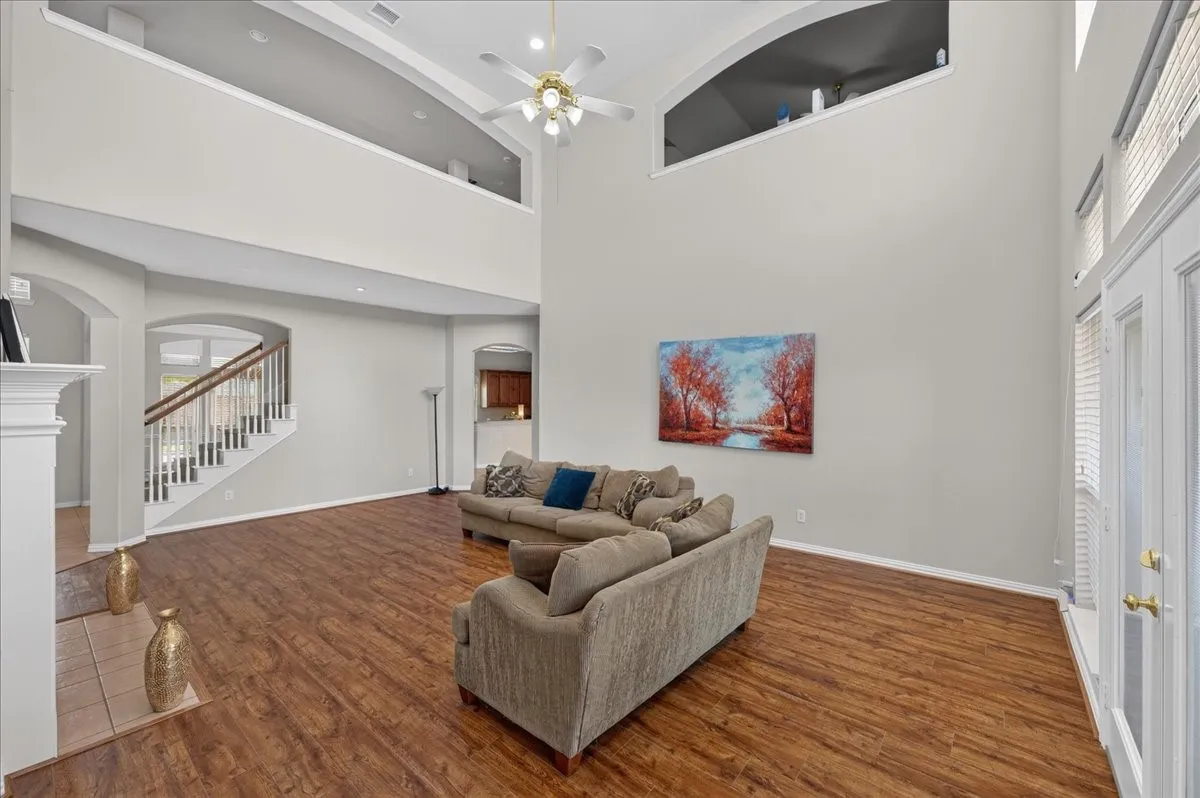 Two-story living area featuring wood-finish flooring, a white mantel, and a ceiling fan