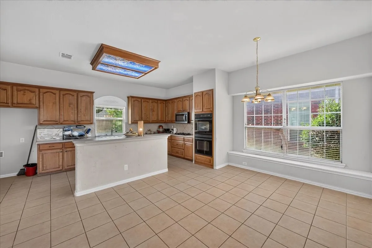 Kitchen and dining area featuring wood cabinetry, stone countertops, built-in appliances, a decorative ceiling light fixture, and tile flooring