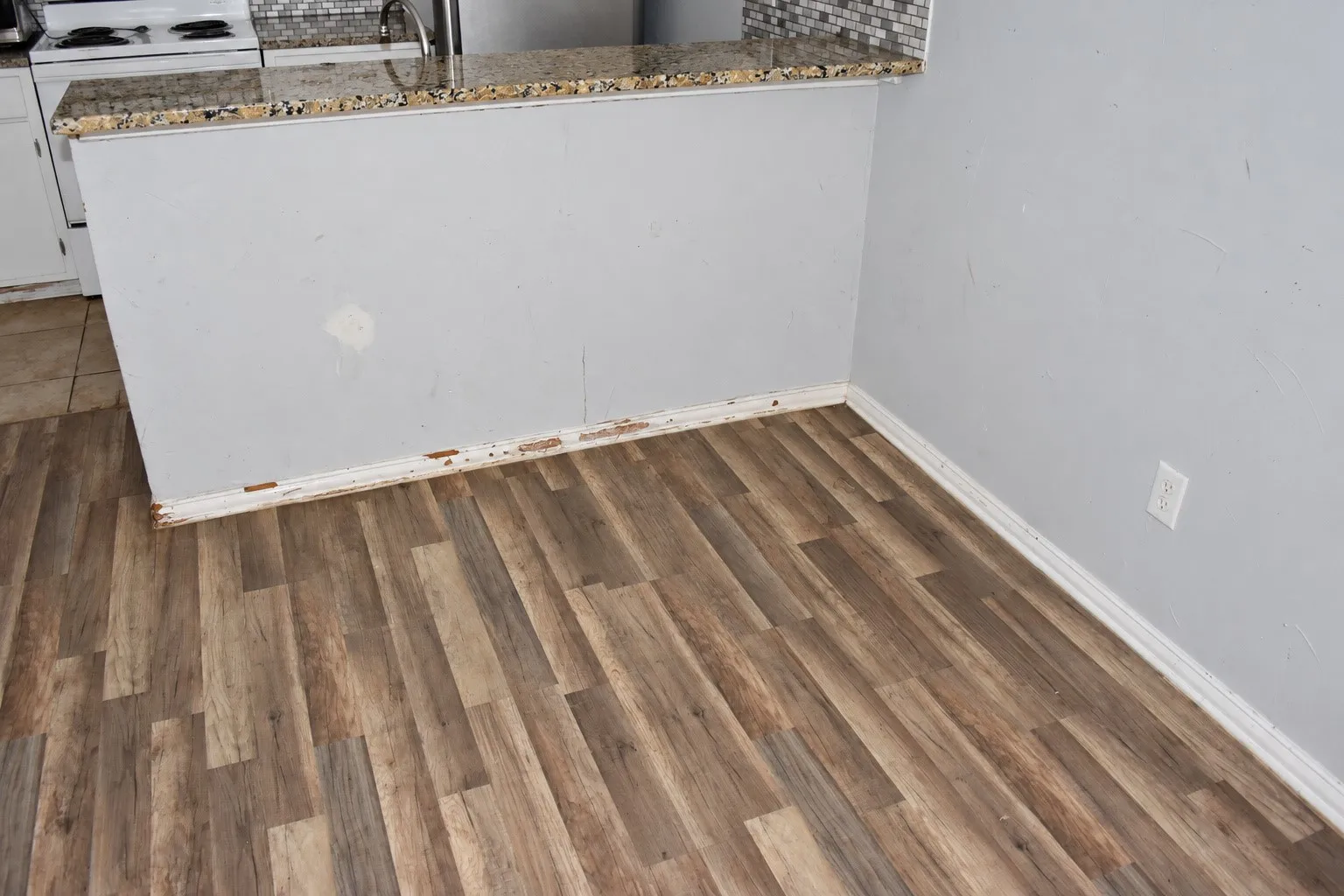 Wood-finish flooring with light gray walls, a partial wall, and white trim