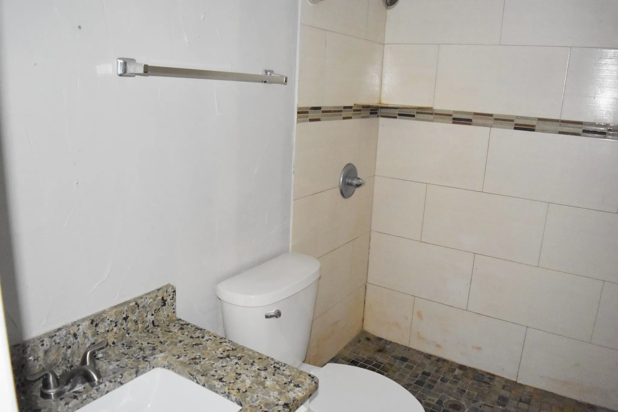 Bathroom featuring a white toilet, chrome fixtures, shower with mosaic tile accent, and a vanity with a stone countertop