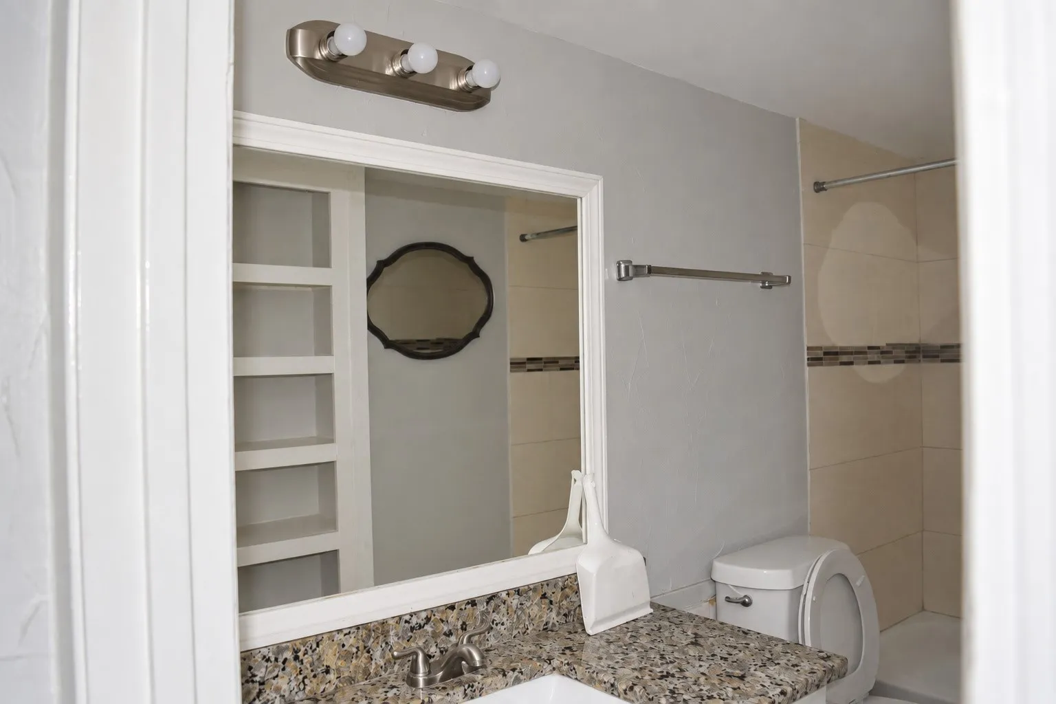 Vanity with a framed mirror, granite-finish countertop, and built-in shelving