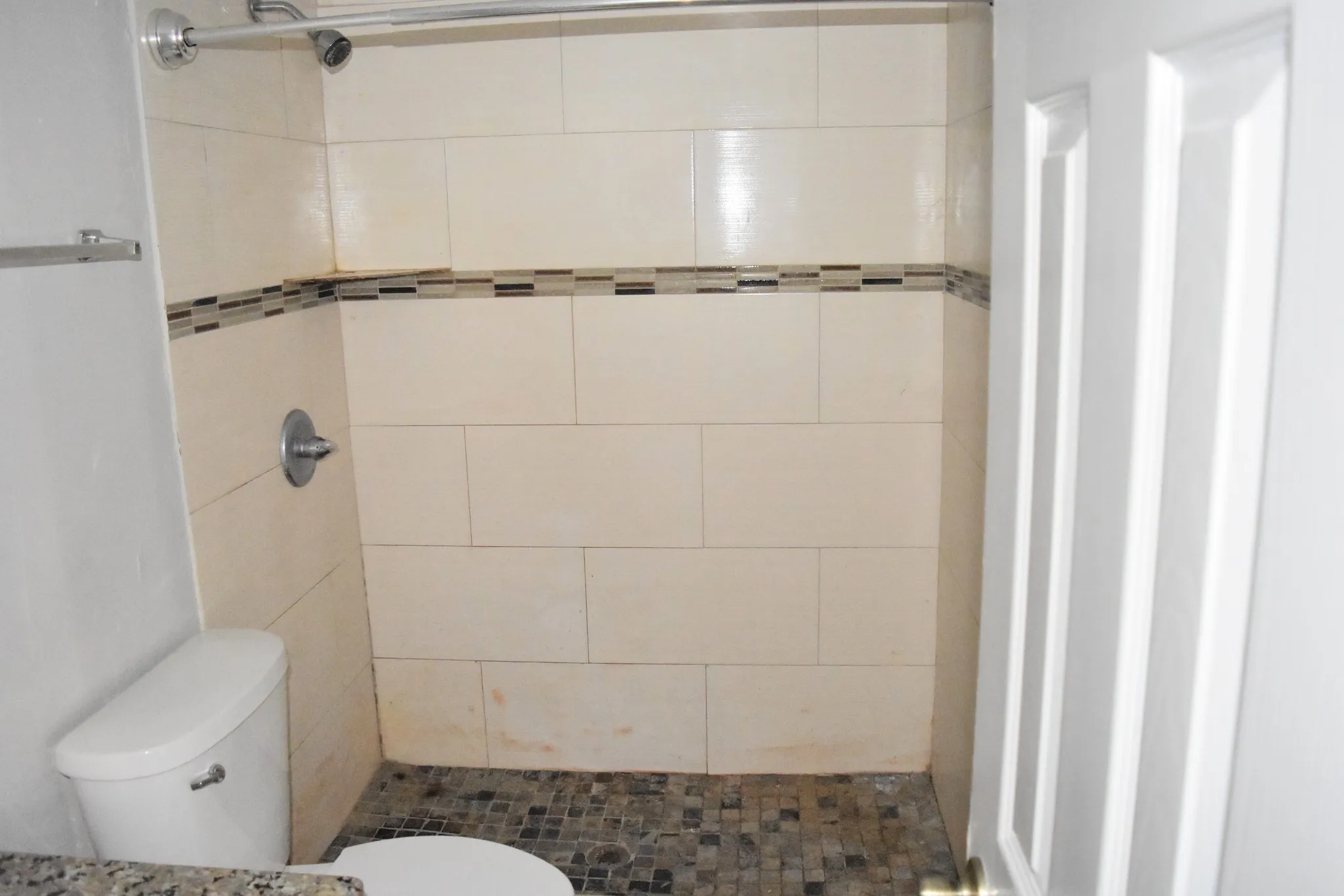 Shower with large-format tile surround and mosaic accent band, pebble-style flooring, and chrome fixtures