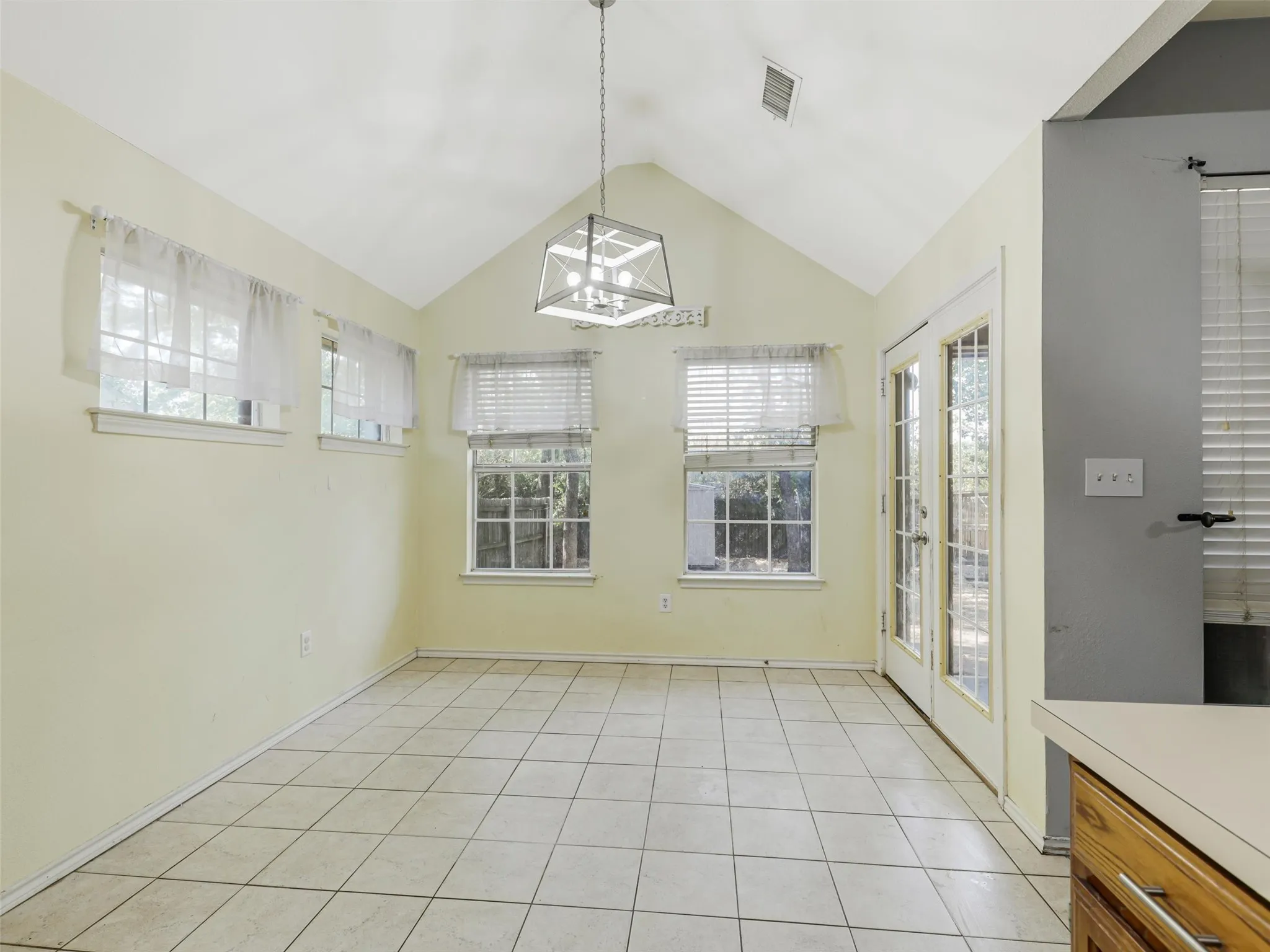 Vaulted ceiling with an angular pendant light fixture, multiple windows, and a French door