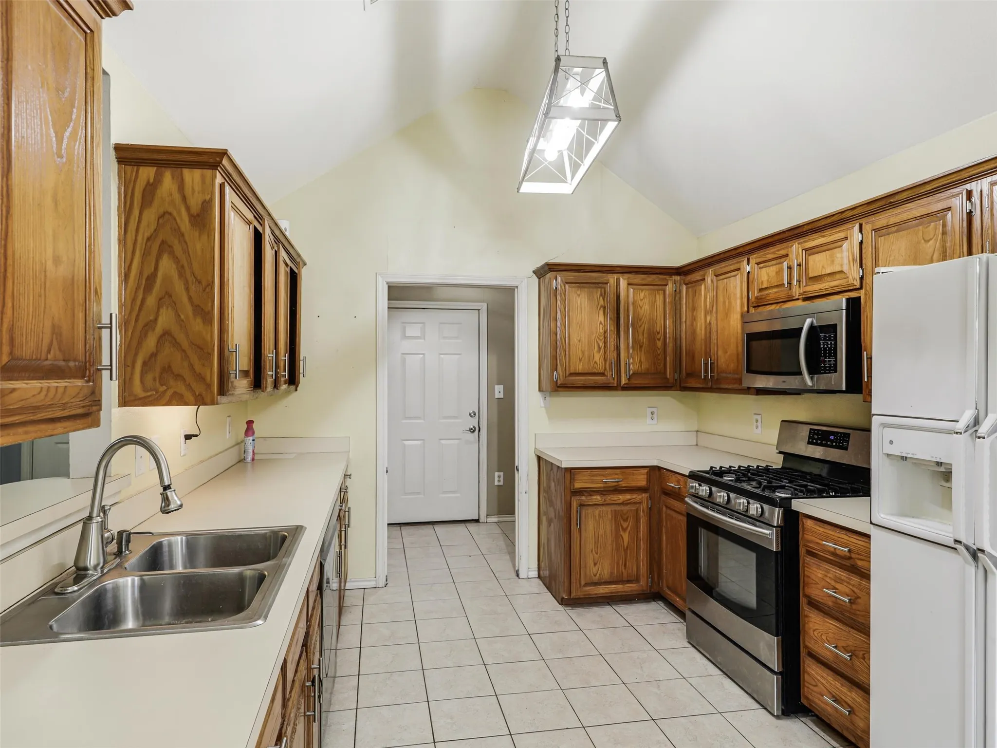 Kitchen featuring wood cabinetry, stainless steel appliances, dual basin sink, and vaulted ceiling