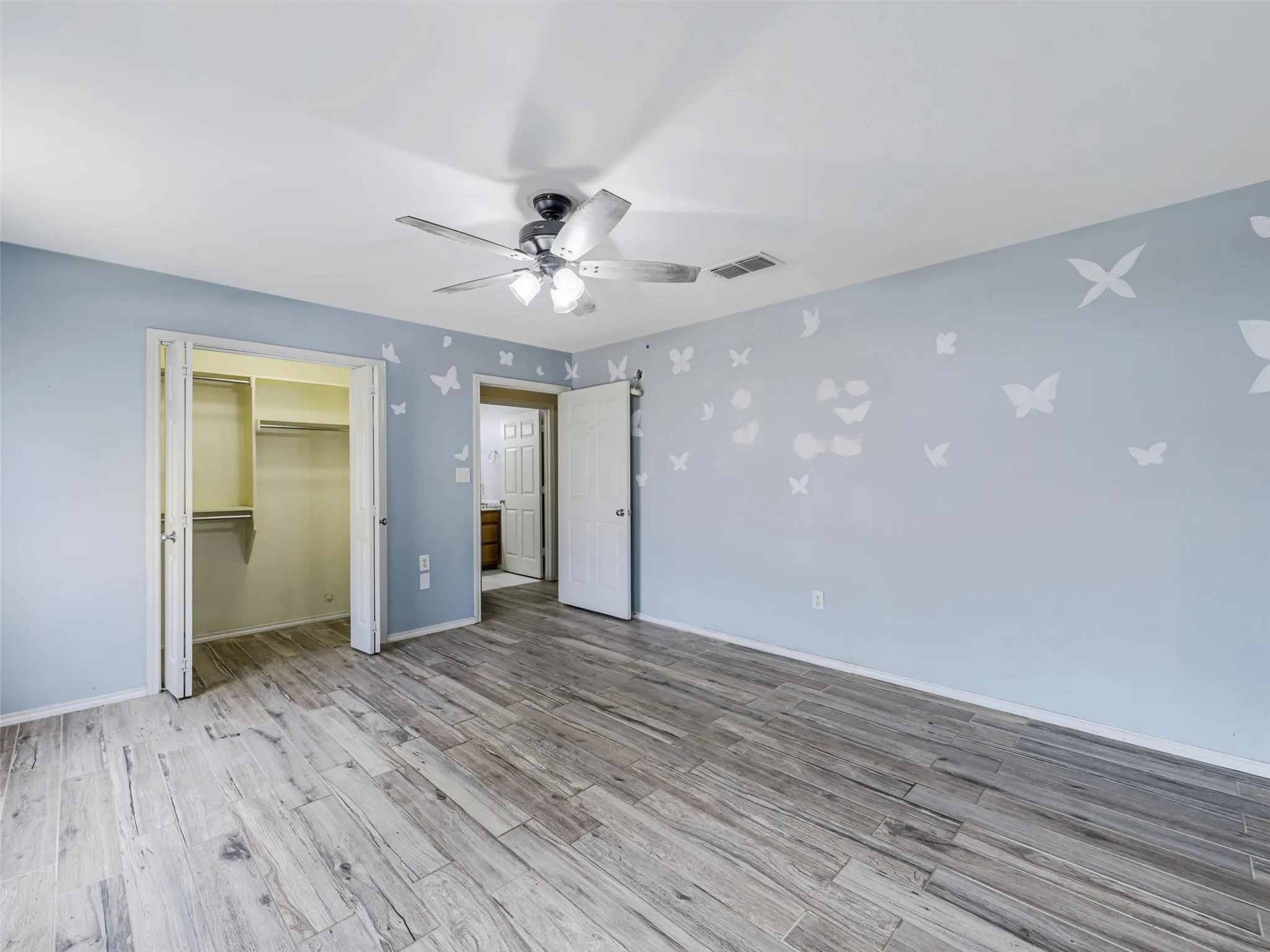 Wood-finish flooring, ceiling fan with integrated lighting, and a built-in closet with shelving and hanging rods