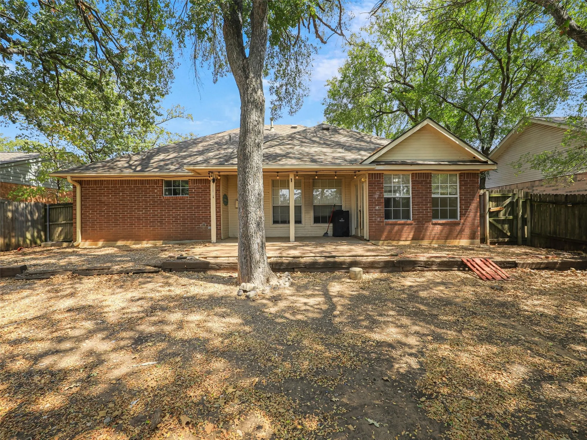 Brick exterior with a gabled roofline, extended concrete patio, and a privacy fence
