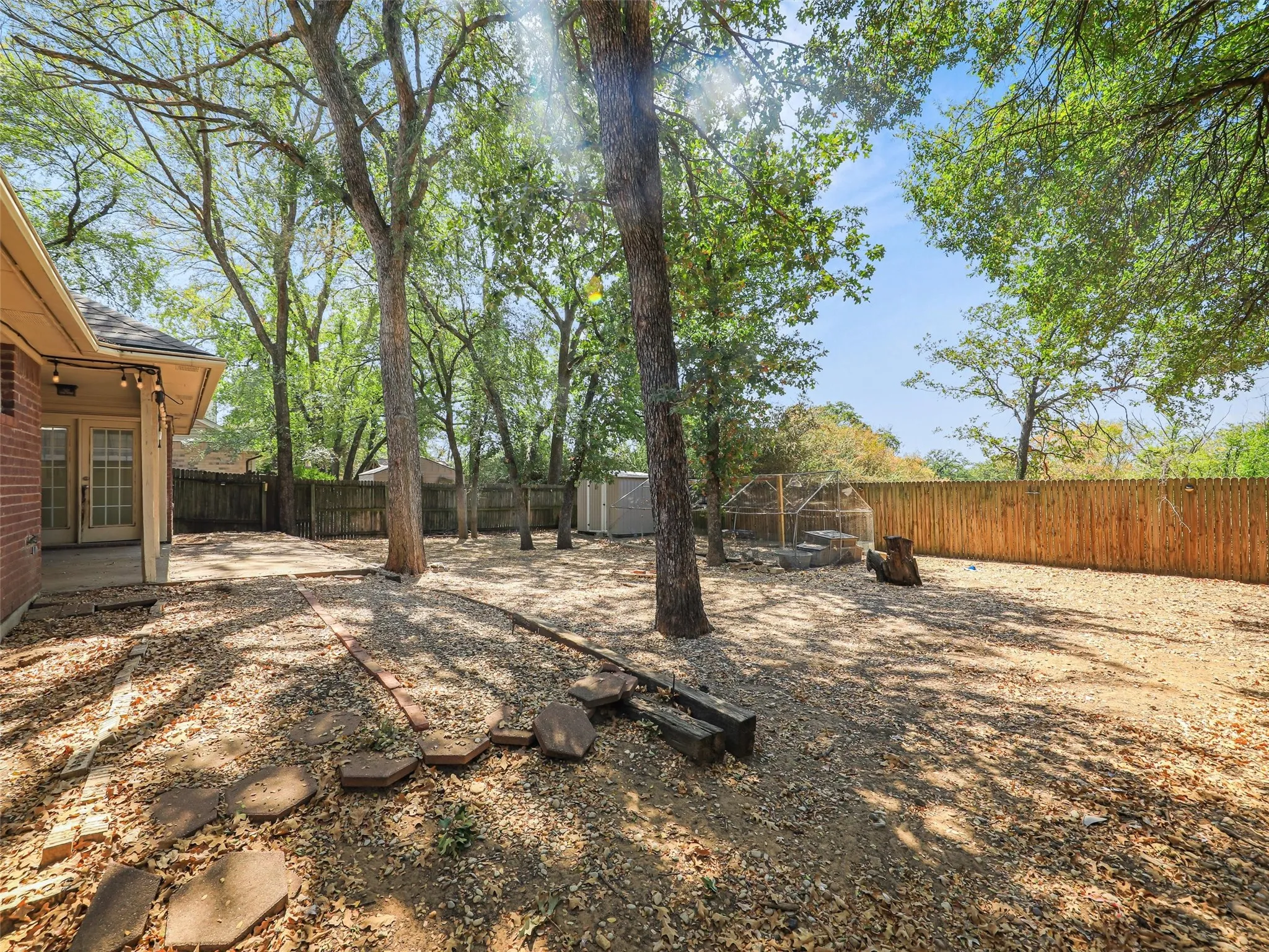 Expansive backyard featuring a wood privacy fence, mature trees, a concrete patio, and a storage shed