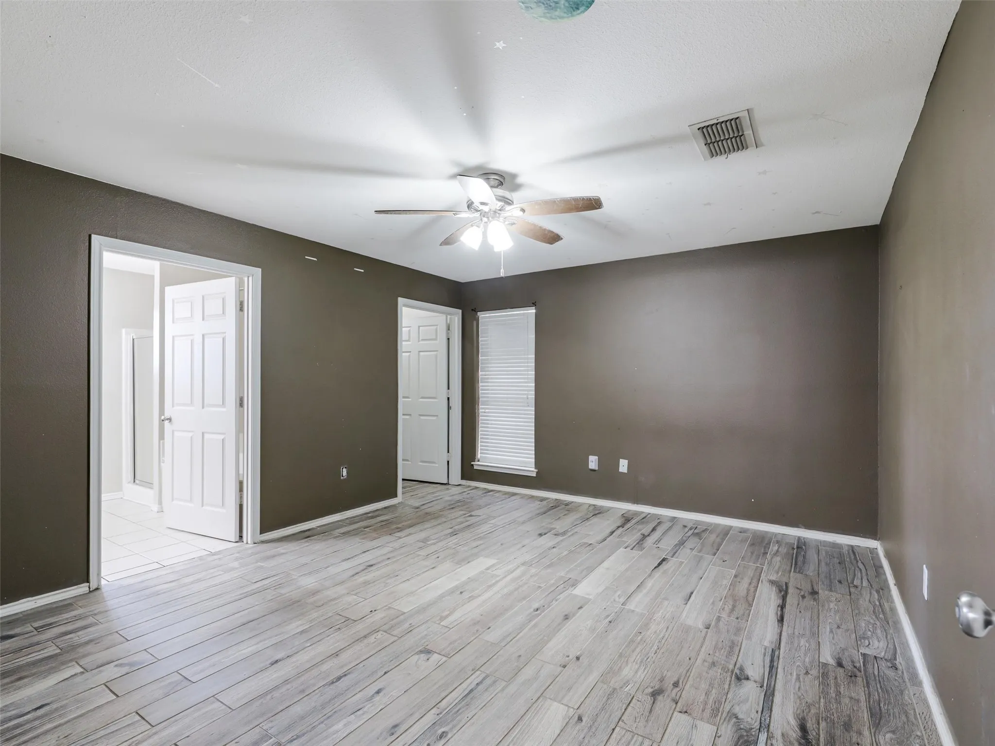 Spacious room featuring wood-finish flooring, ceiling fan with integrated lighting, and multiple panel doors