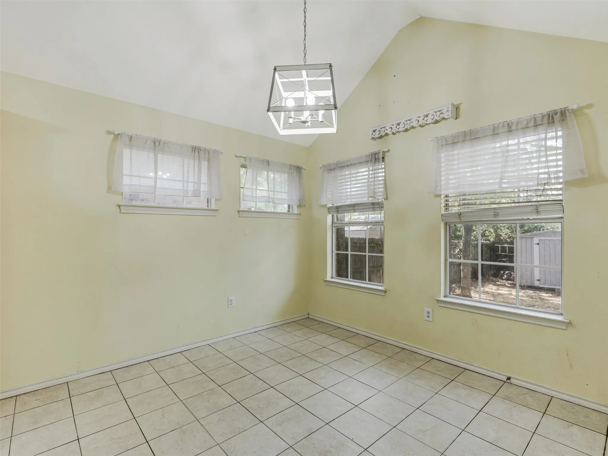 Vaulted ceiling, tiled flooring, multiple windows, and a hanging light fixture