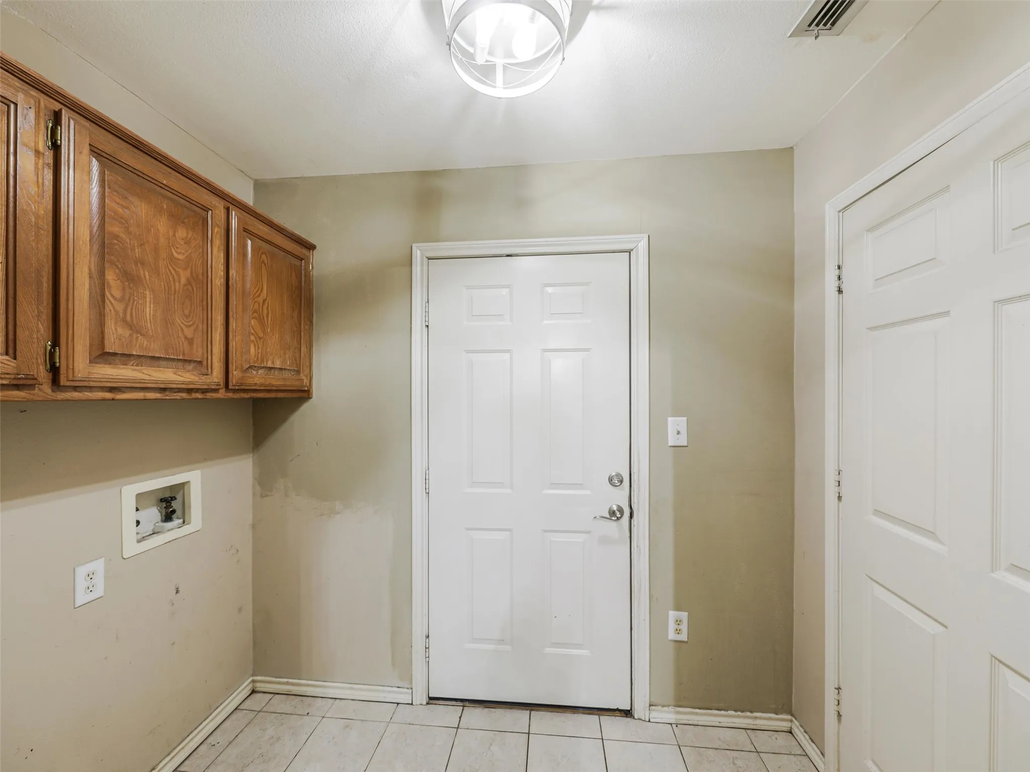 Hardwood-finish cabinetry, white paneled door, ceiling-mounted light fixture, and tile flooring