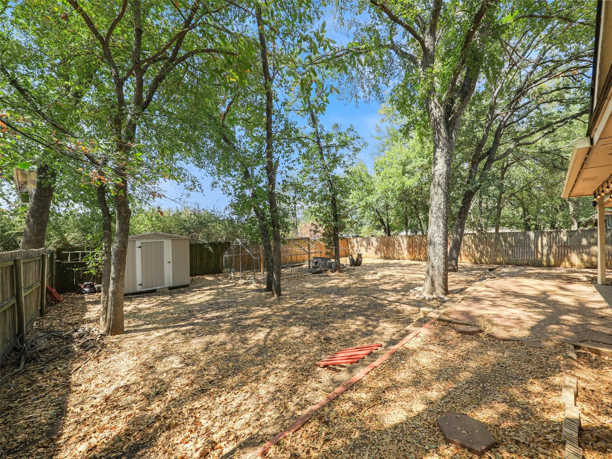 Spacious backyard with mature trees, fenced perimeter, and a storage shed