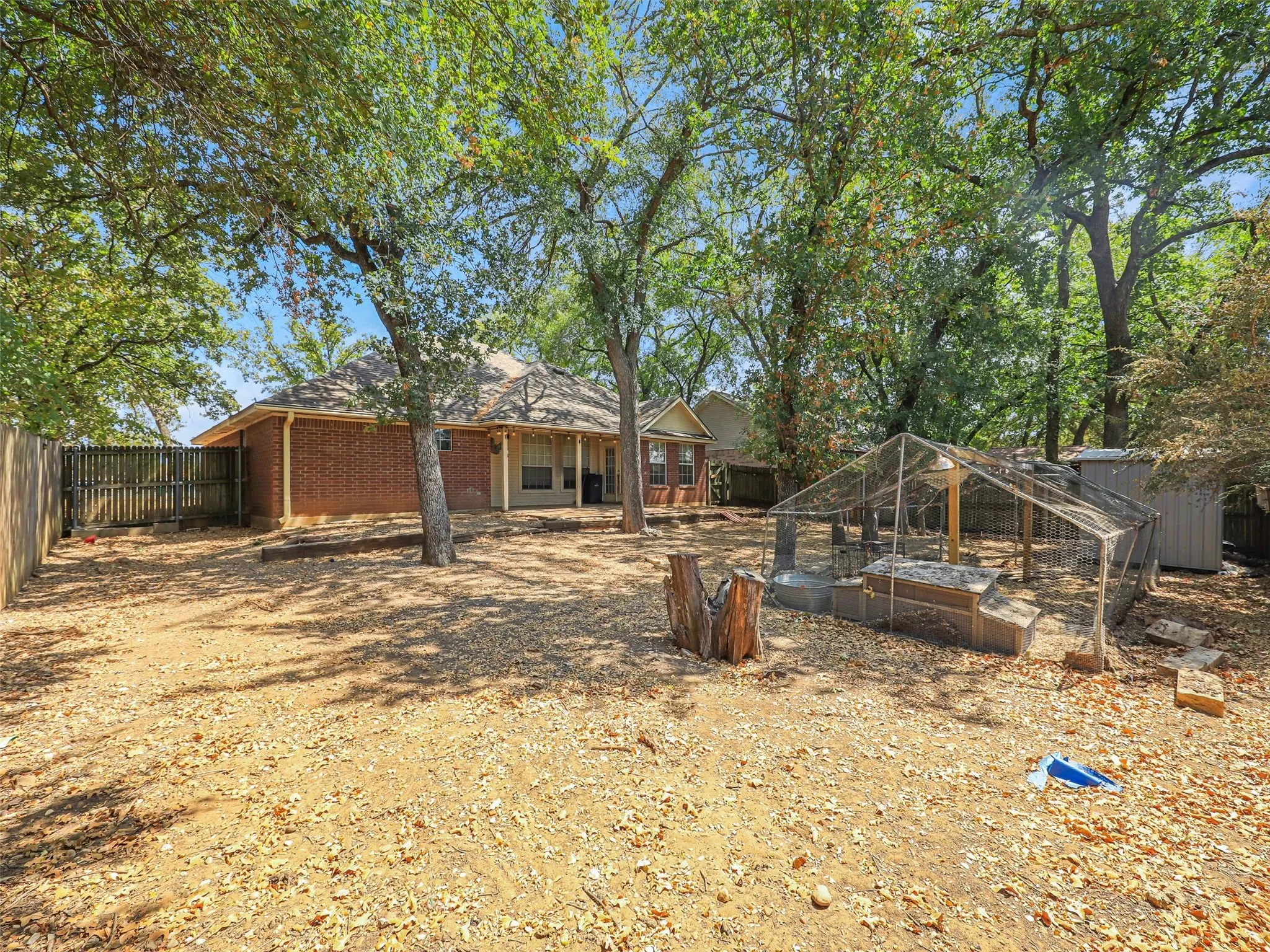 Expansive backyard with a full privacy fence, mature trees, and a red brick exterior