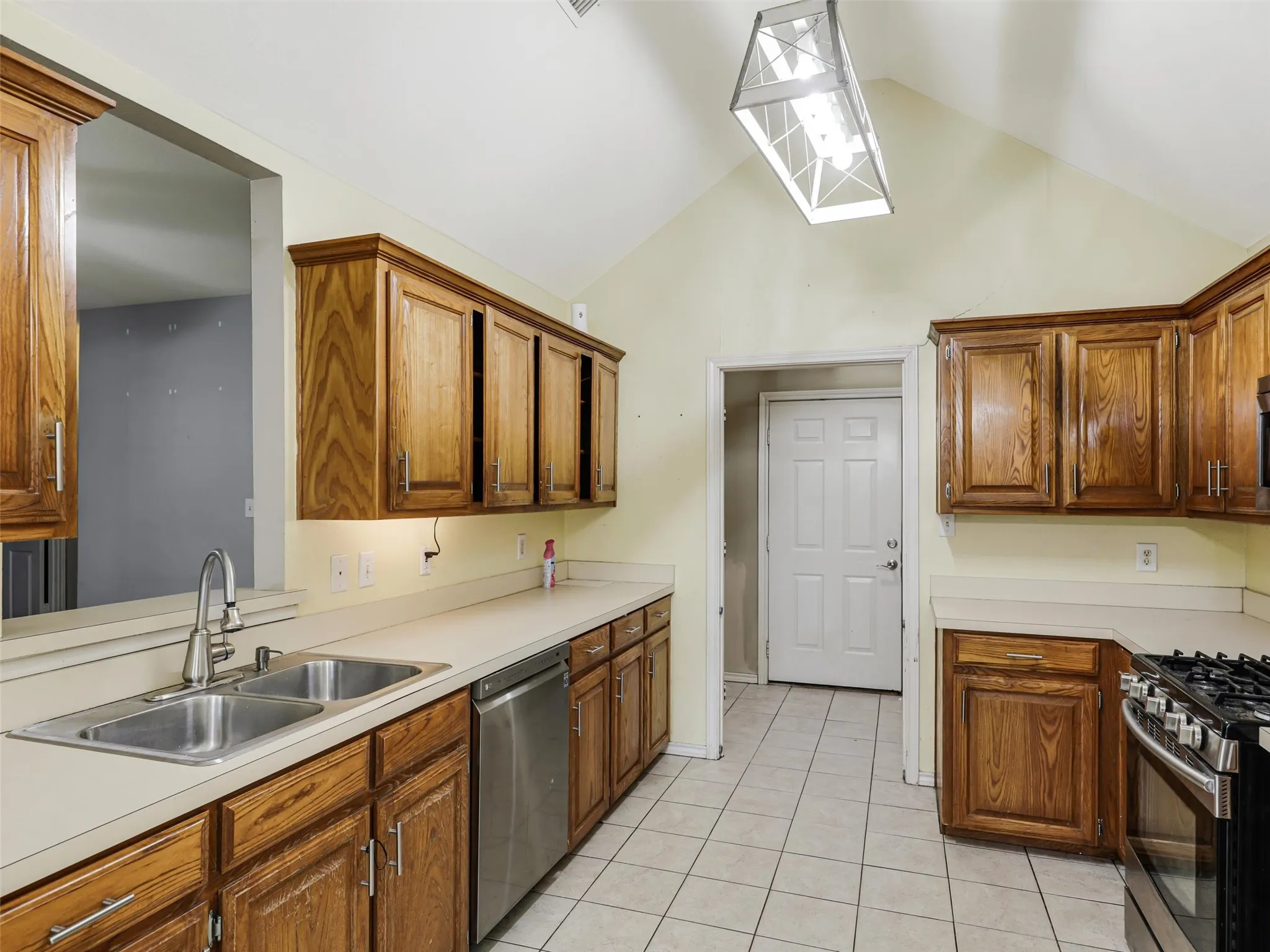 Kitchen featuring ample wood cabinetry, a dual basin stainless steel sink, stainless steel dishwasher, and a gas range