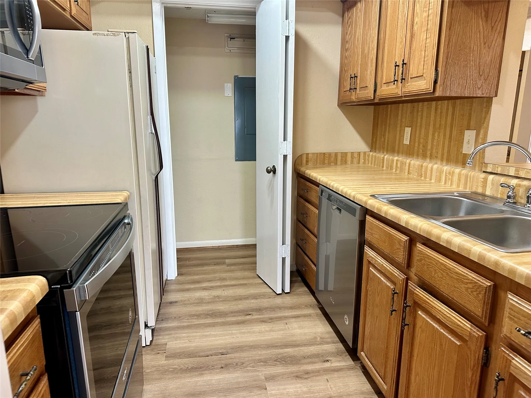 Wood-finish flooring, wood cabinetry with dark hardware, dual basin stainless steel sink, stainless steel dishwasher, and built-in microwave