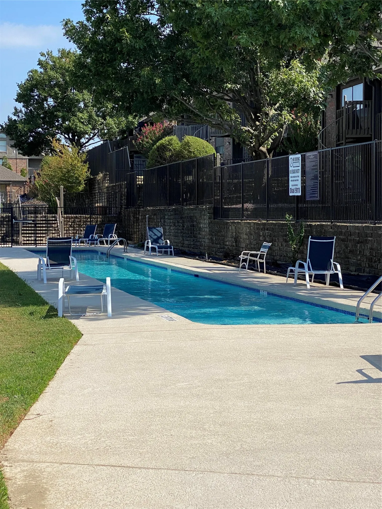 Rectangular outdoor swimming pool featuring a concrete deck and surrounding metal fencing