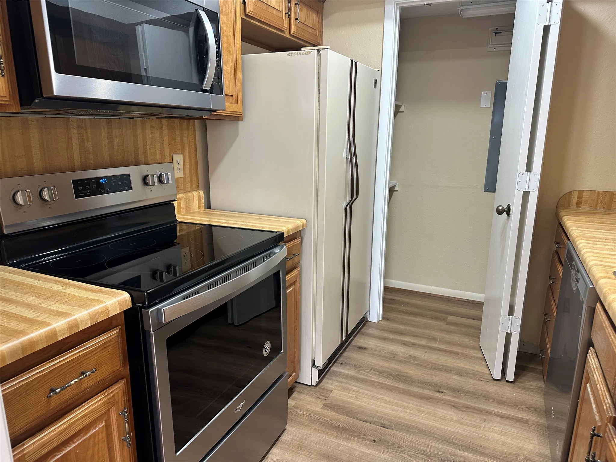 Wood-finish flooring, stainless steel microwave, stainless steel electric range, oak cabinetry, and laminate countertops