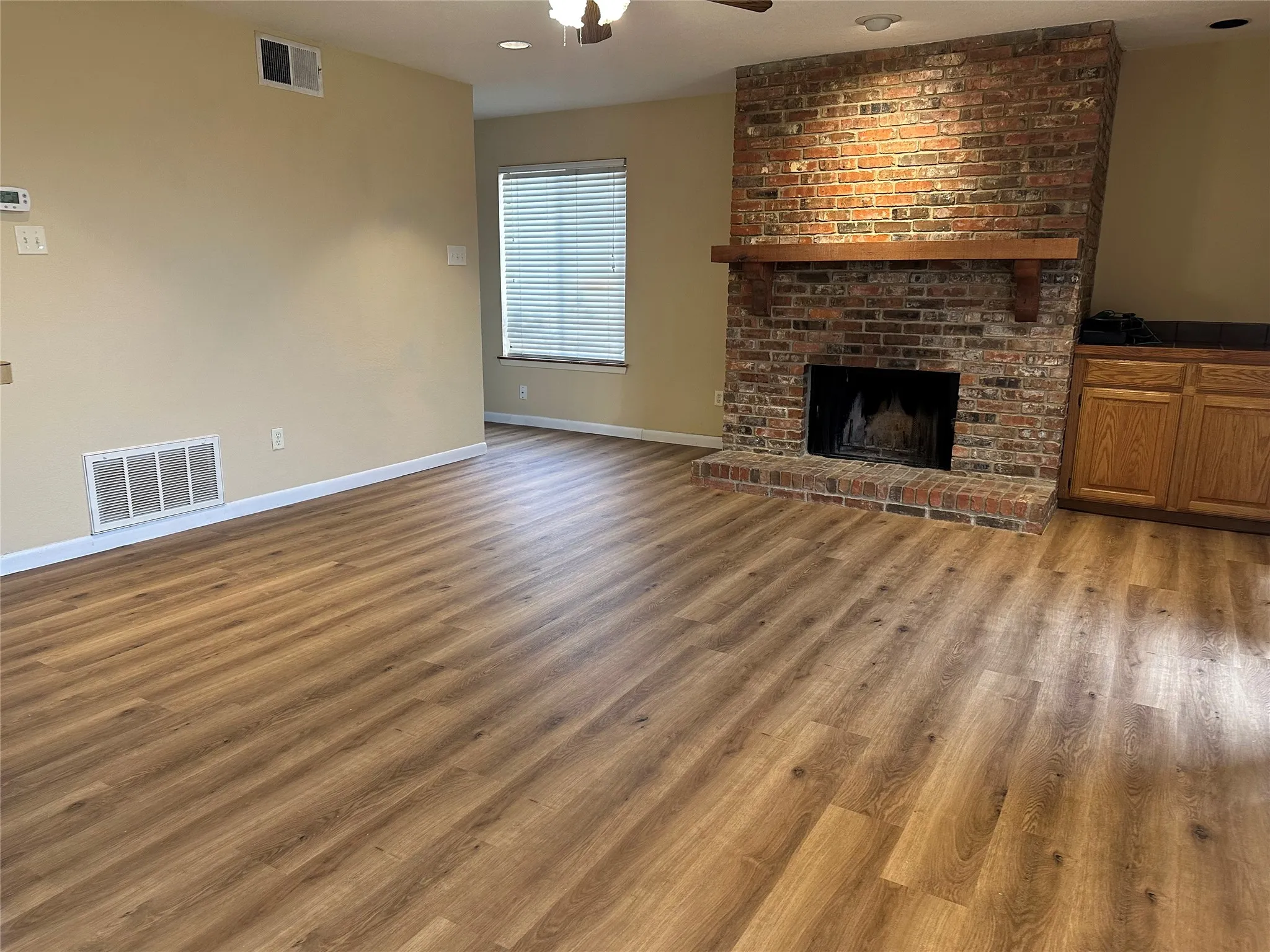 Spacious room featuring wood-finish flooring, a brick fireplace with a wood mantle, and a built-in cabinet