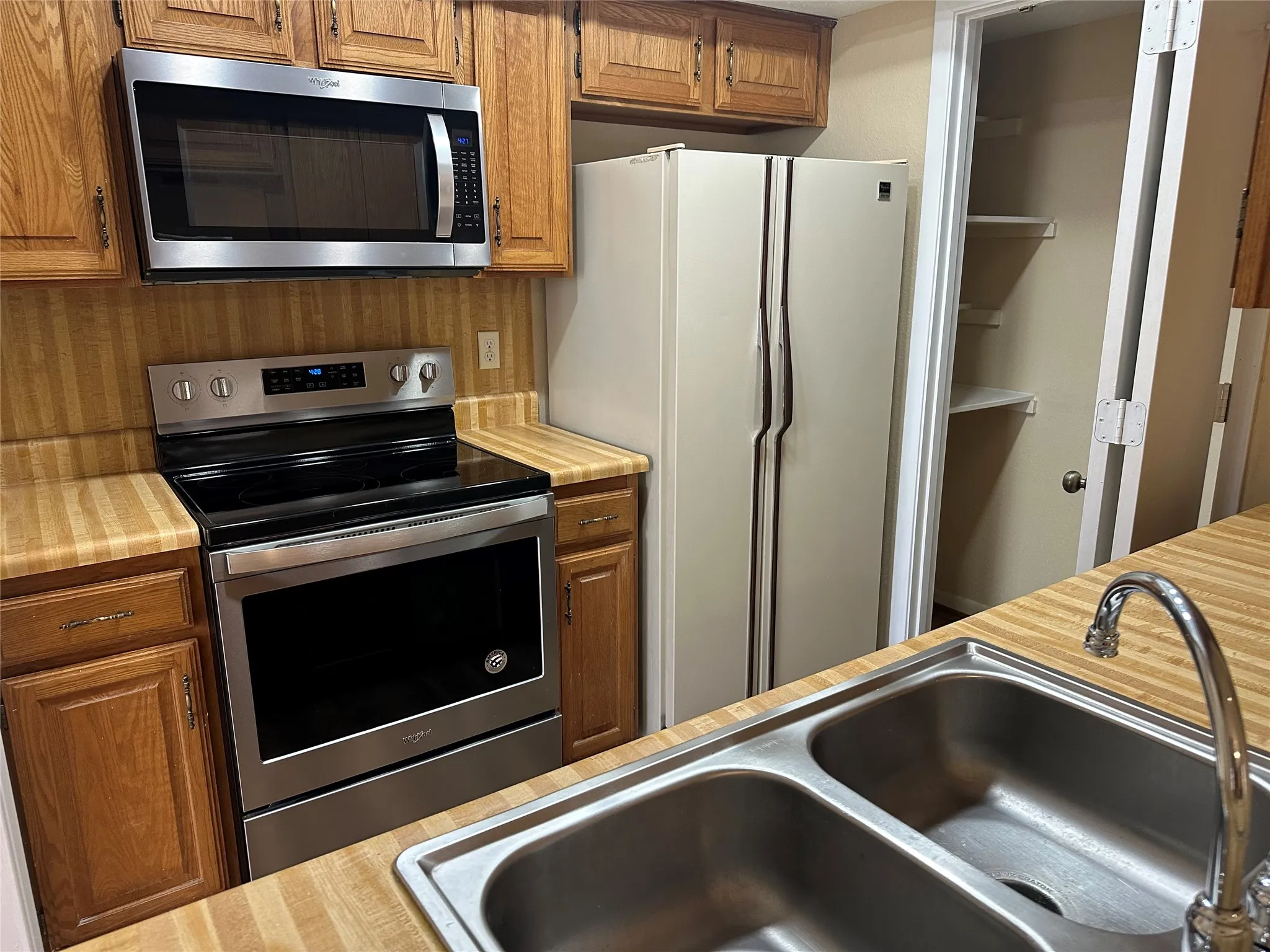 Stainless steel microwave and range, wood-finish countertops, wood cabinetry, and a double basin stainless steel sink with a chrome faucet