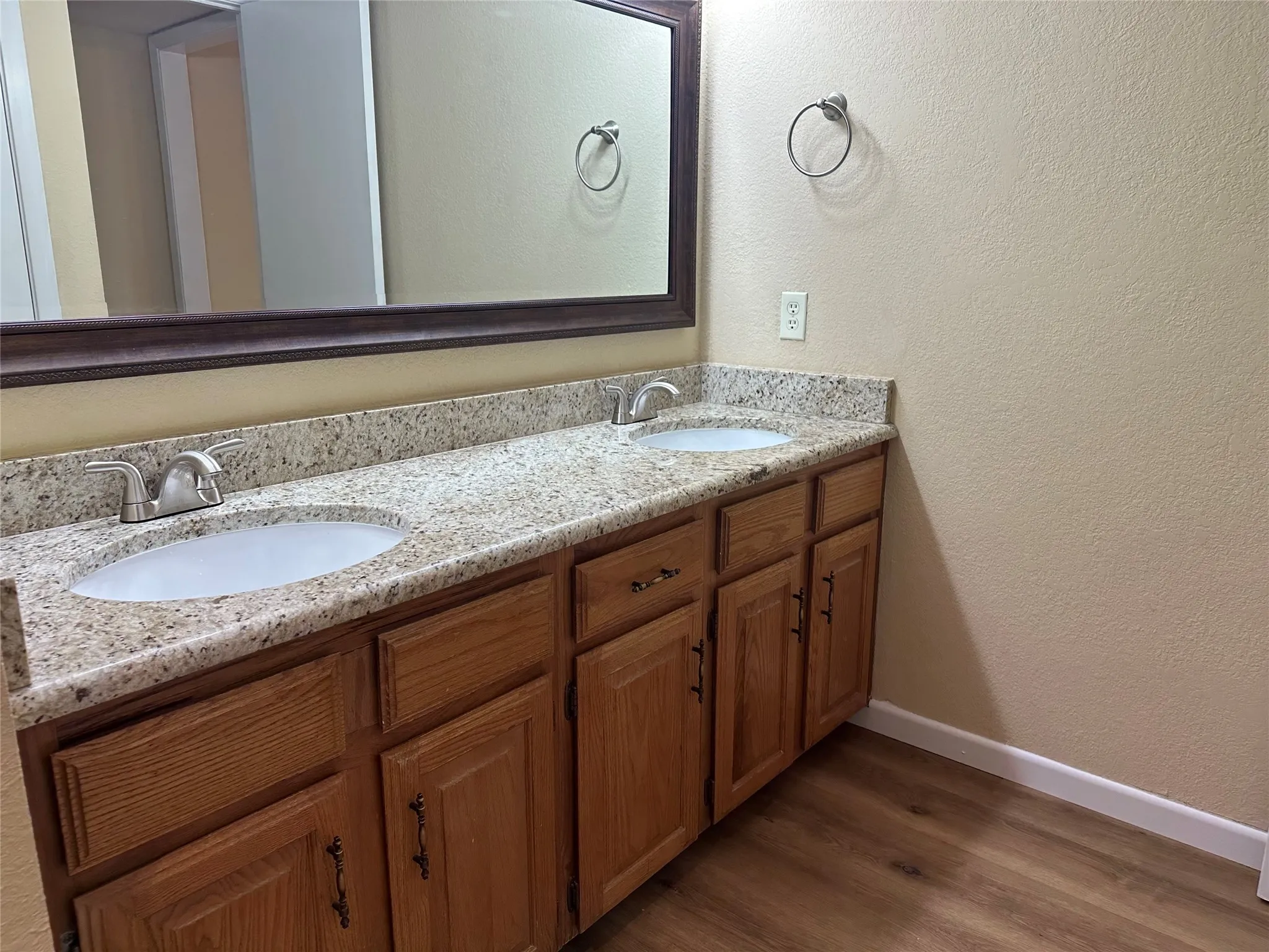 Dual vanity with granite-style countertop, wood-finish cabinetry, and wood-finish flooring