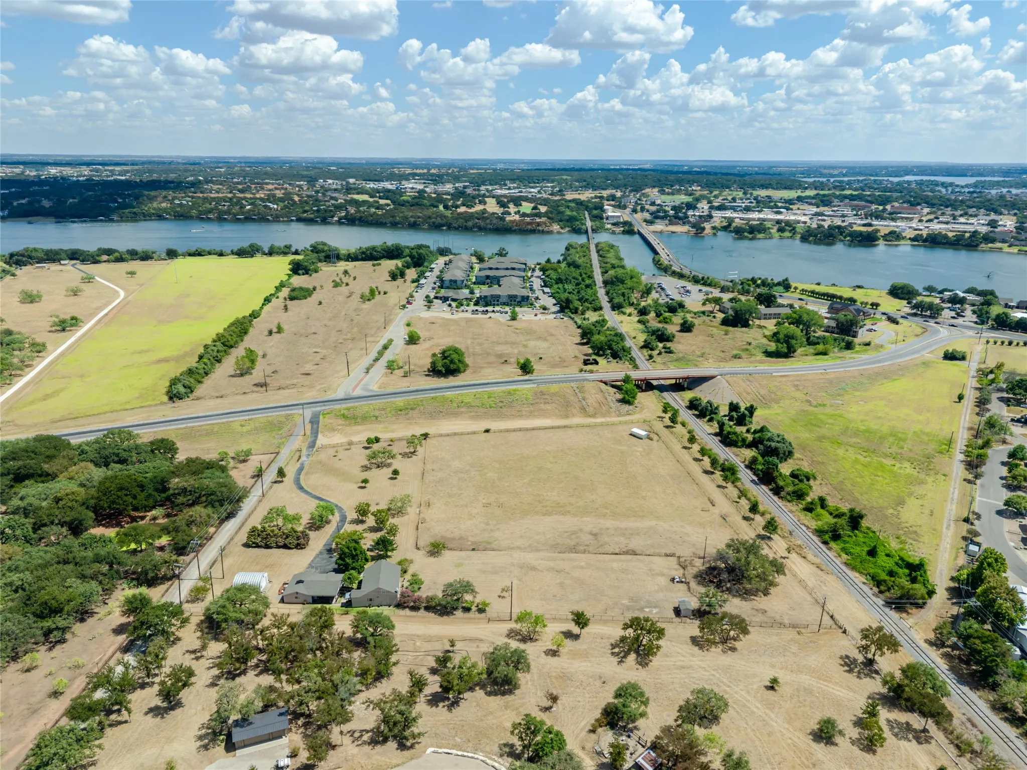 Expansive land parcel featuring open fields, surrounding natural foliage, and proximity to a large body of water with a distant bridge