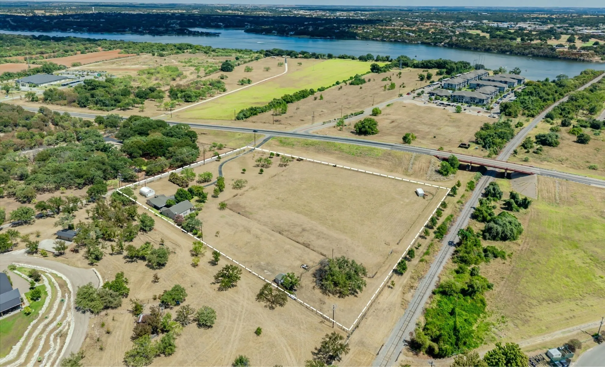 Expansive property featuring a waterfront backdrop, established structures, mature trees, and a defined boundary