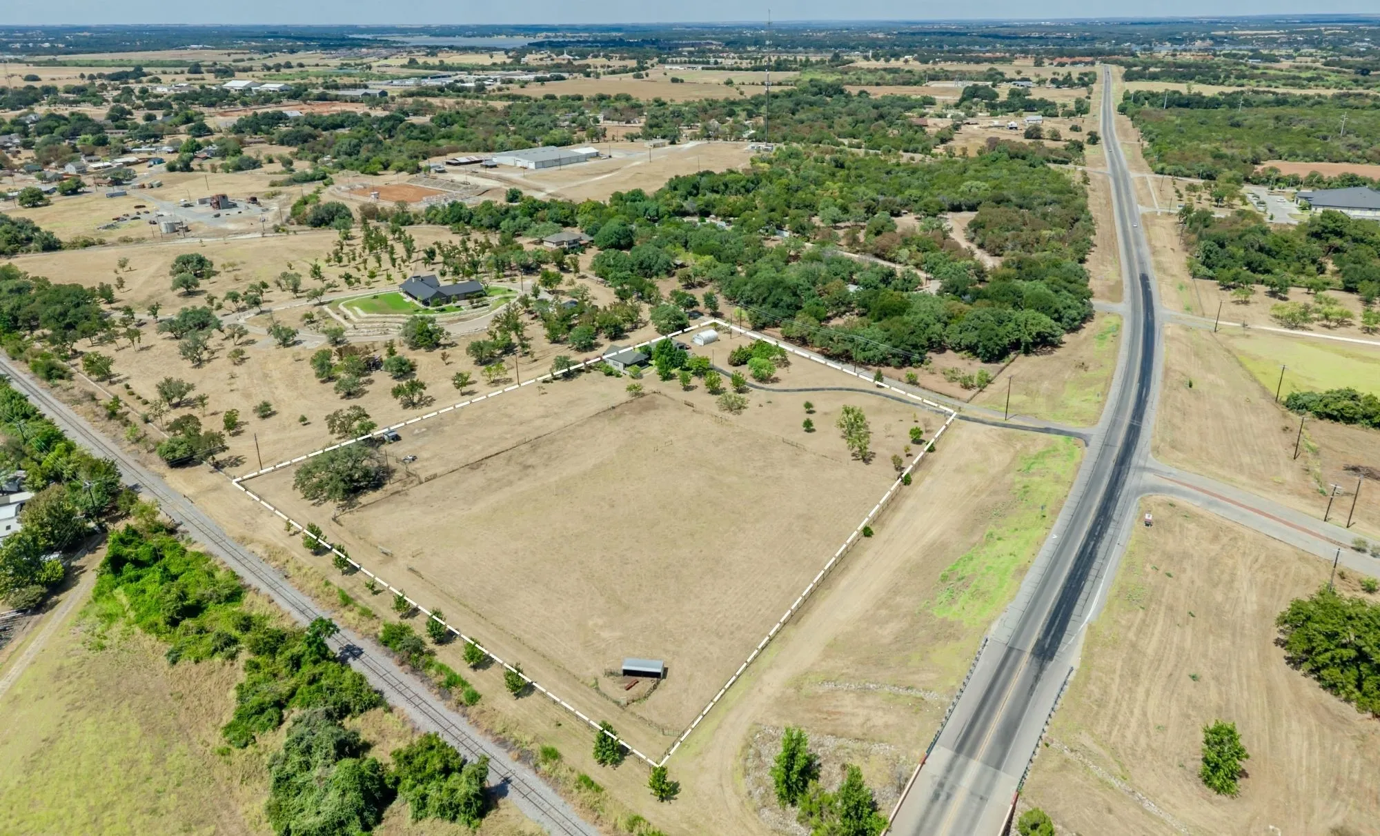 Expansive acreage featuring a broad, flat terrain, a paved road, and a cluster of mature trees