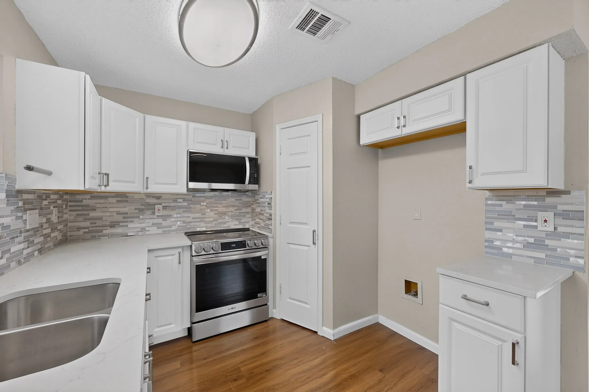 White cabinetry, stainless steel appliances, patterned tile backsplash, wood-finish flooring, and a double basin sink