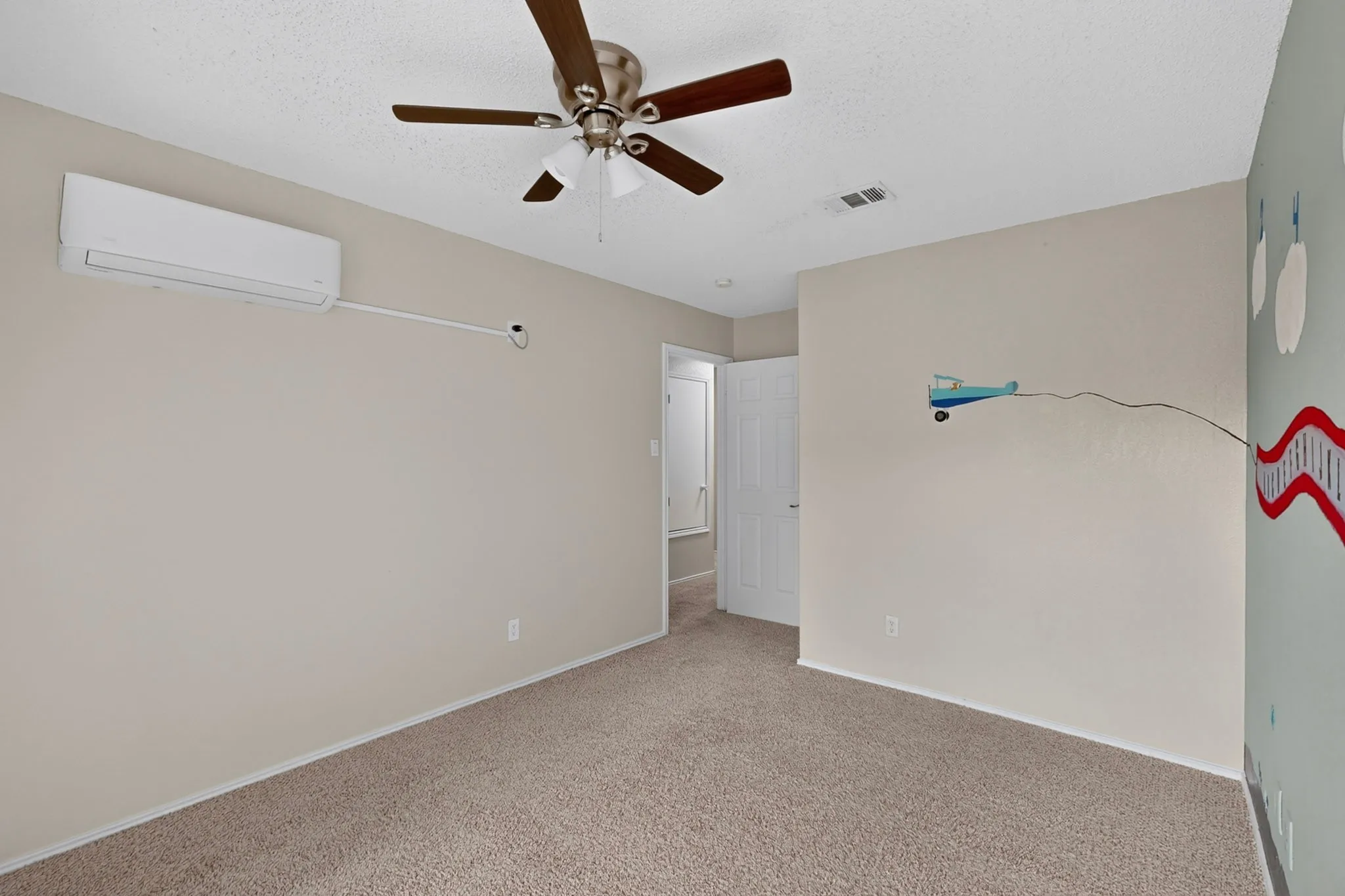 Carpeted flooring with a ceiling fan, a wall-mounted air conditioning unit, and a white interior door