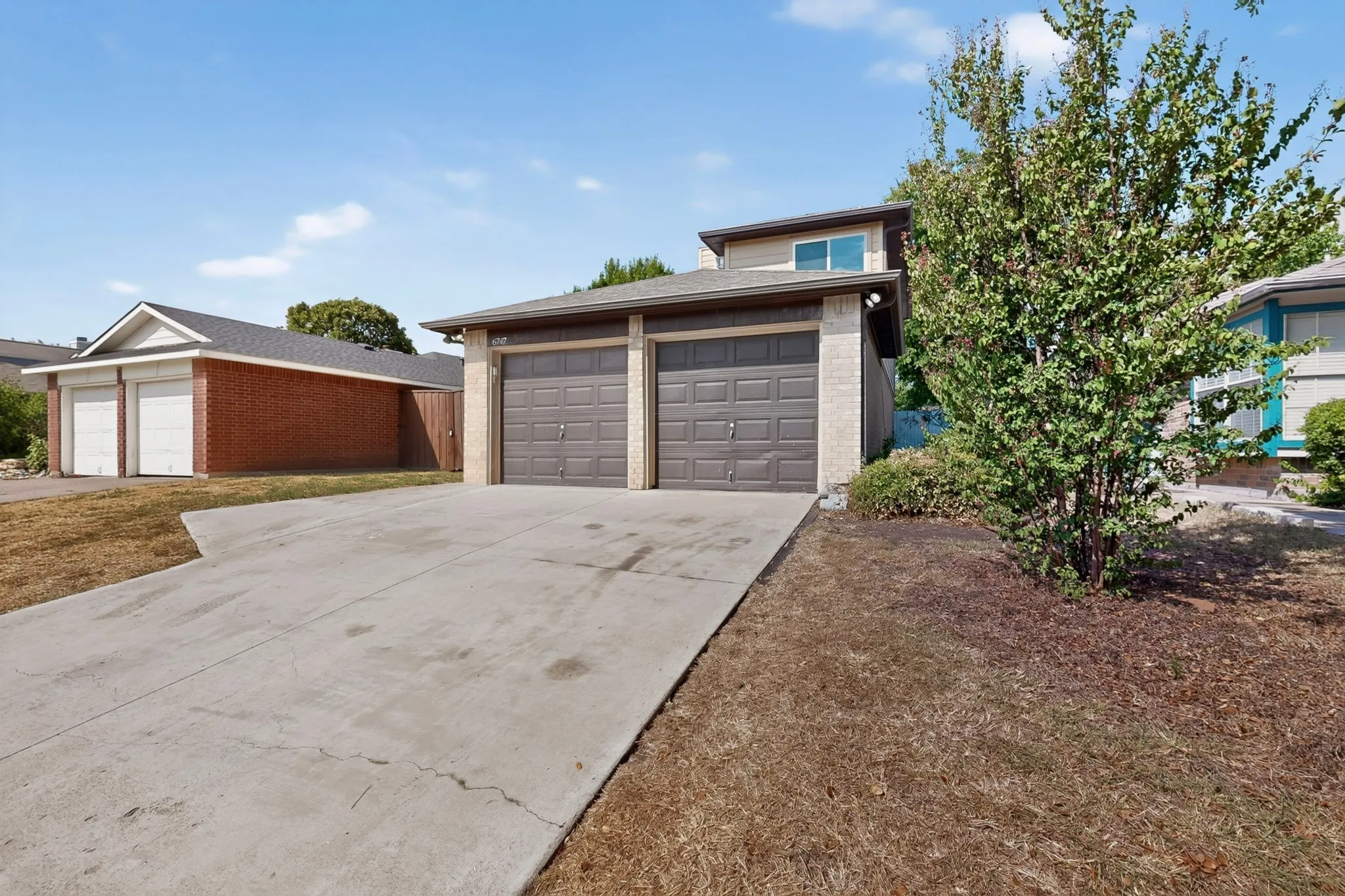 Two-car garage with panel doors, concrete driveway, and mature landscaping